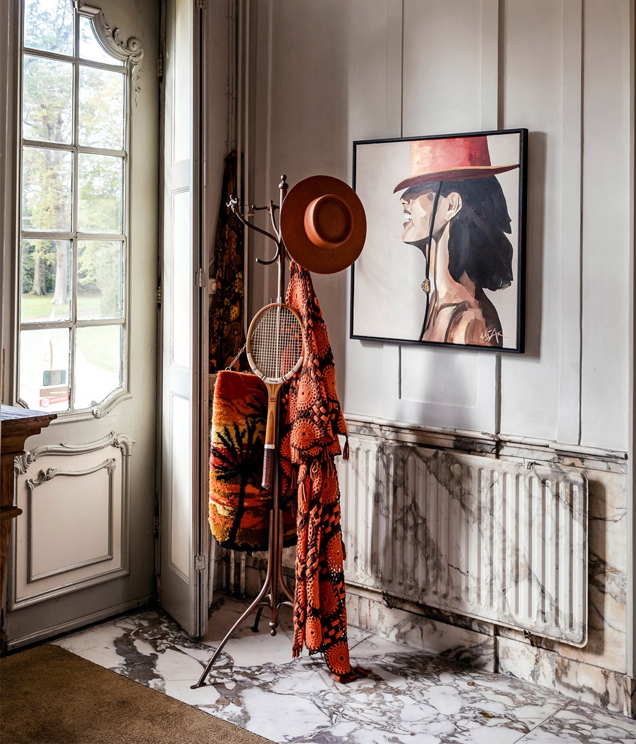 Achter de voordeur een marmeren vloer en balustrade met trompe-l’oeil effect: pas in tweede instantie wordt de radiator zichtbaar achter de klassieke Thonet-kapstok met vintage stukken. Het schilderij is The Red Hatter van Eliane Douglas. vtwonen 01-2021 | productie Roos Stalpers &amp; Fee van ’t Veen | fotografie Ernie Enkelaar