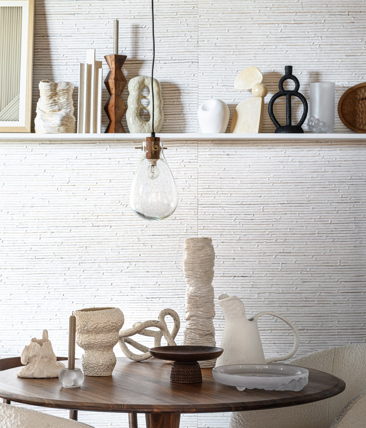 Behang Cabestan van Nobilis, 110 cm breed, per meter (wva.nl). Lamp (hm.com). Bouclé stoel Noelle (karwei.nl). Stoel walnoothout en leer (kasstoor.nl). Walnoothouten tafel, 120 cm (Ø) (demachinekamer.nl). Op tafel: wit afvalzak-object Josefin Zachrisson (theodeto.com). Melkglazen kandelaar (bolia.com). Vaas met textuur (studio-yen.com). Organisch object Emeli Höcks (theodeto.com). Hoge vaas Wobbly (2222studio.com). Houten etagère (kasstoor.nl). Keramieken kan (njoyliving.nl). Melkglazen schaal (bolia.com). Op plank: poster in lijst (hkliving.nl). Wit object lijnen, kandelaar (zarahome.com). Sculptuur met openingen (studio-yen.com). Wit object met deuk Atelier Armand (theodeto.com). Keramieken vaas Wobbly, object met drie elementen (2222studio.com). Zwarte kandelaar (njoyliving.nl). Melkglazen vaas (bolia.com). Houten dienblad (kasstoor.nl). vtwonen 13-2020 | styling Daniëlle Verheul | fotografie Sjoerd Eickmans