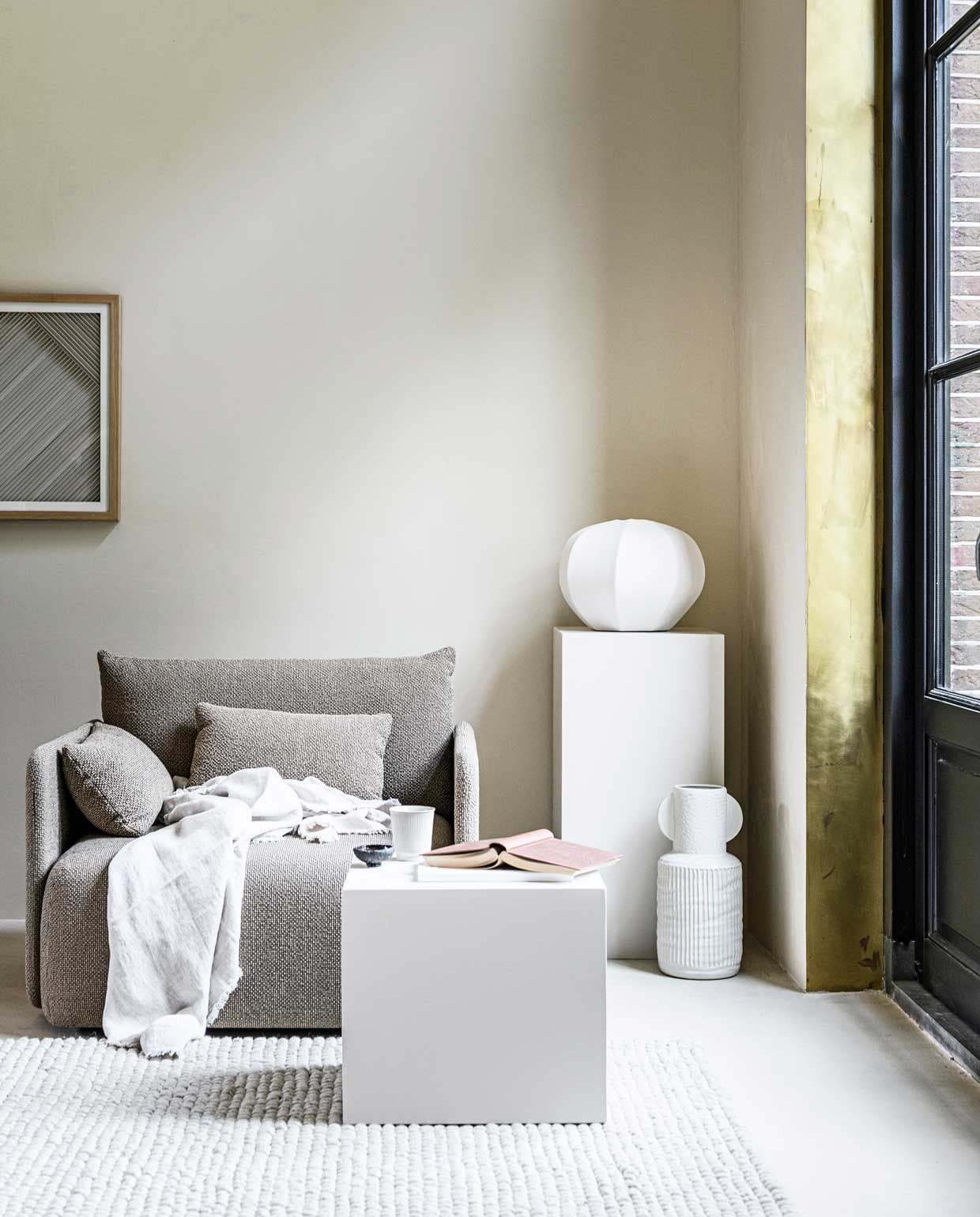 Kleur op de muur Mikonos van We Are Wow Makers, prijs op aanvraag, vloer Urban Clay in de kleur Ibiza, prijs op aanvraag (anoukb.com). Sofa Offset van Menu, Poster Layered Paper in houten lijst van HKliving € 75,-, witte bolvaas Cyrus van Urban Nature Culture € 119,-, vloerkleed Peas van Hay, 240×170 cm € 645,- (vtwonen.nl). Witte vaas met oren € 54,95, mok € 6,25 (loods5.nl). Linnen deken € 79,99 (zarahome.com). Boeken en zwart schaaltje privébezit.