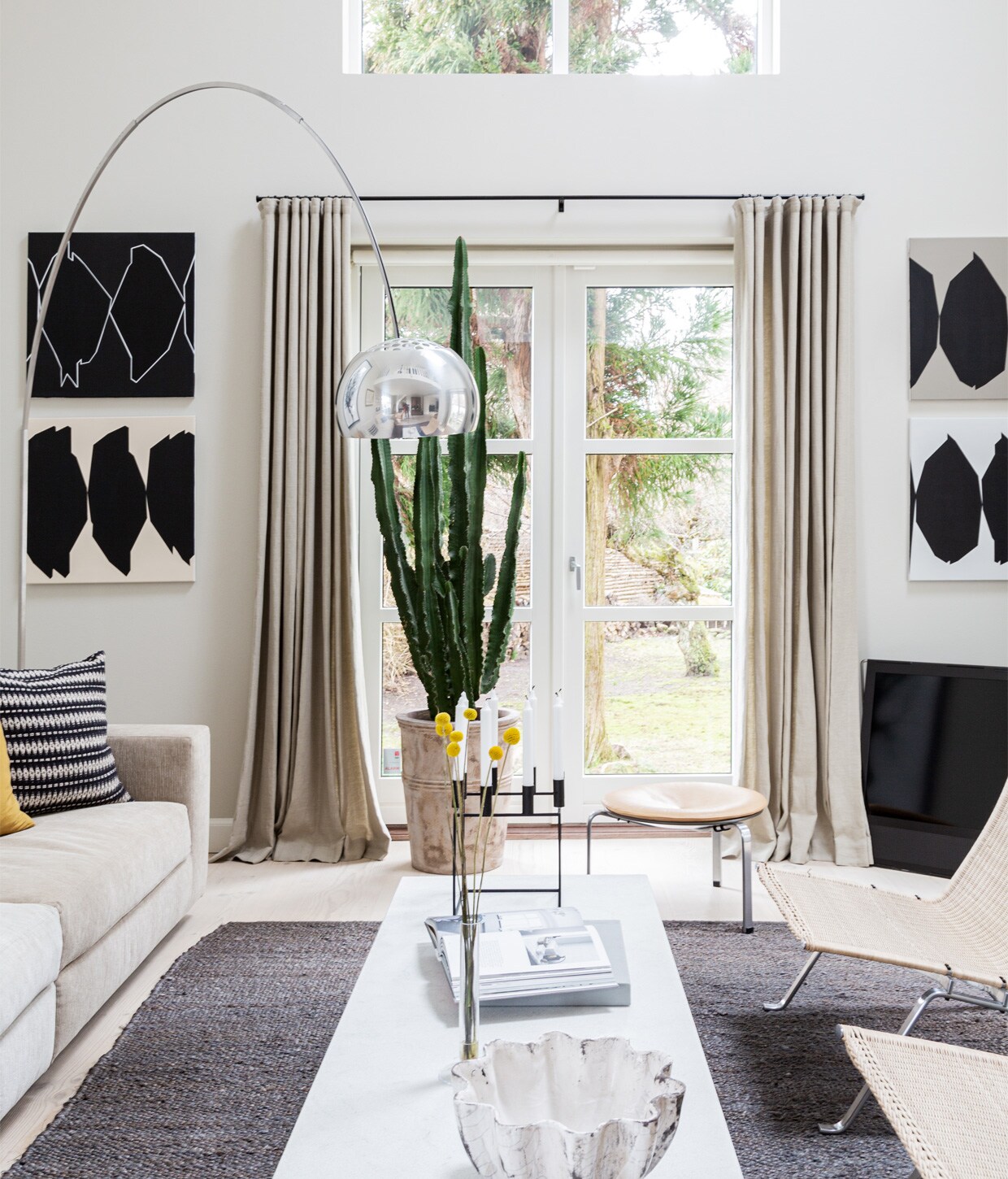 Muurverf Shaded White van Farrow &amp; Ball. Bank Eilersen. Kussens Tapet-Cafe. Koffietafel PK62 Poul Kjærholm voor Fritz Hansen. Lamp Arco van Flos. Kunstwerk in kleur Egill Jacobsen. Schilderij Cathrine Raben Davidsen. Vloerkleed Tine K Home. Kaarsenstandaard Mogens Lassen. vtwonen 13-2020 | Productie Living Inside | Styling Henrietta Sharma | Fotografie Annita Behrendt | Tekst Adeline mans, Pia Olsen