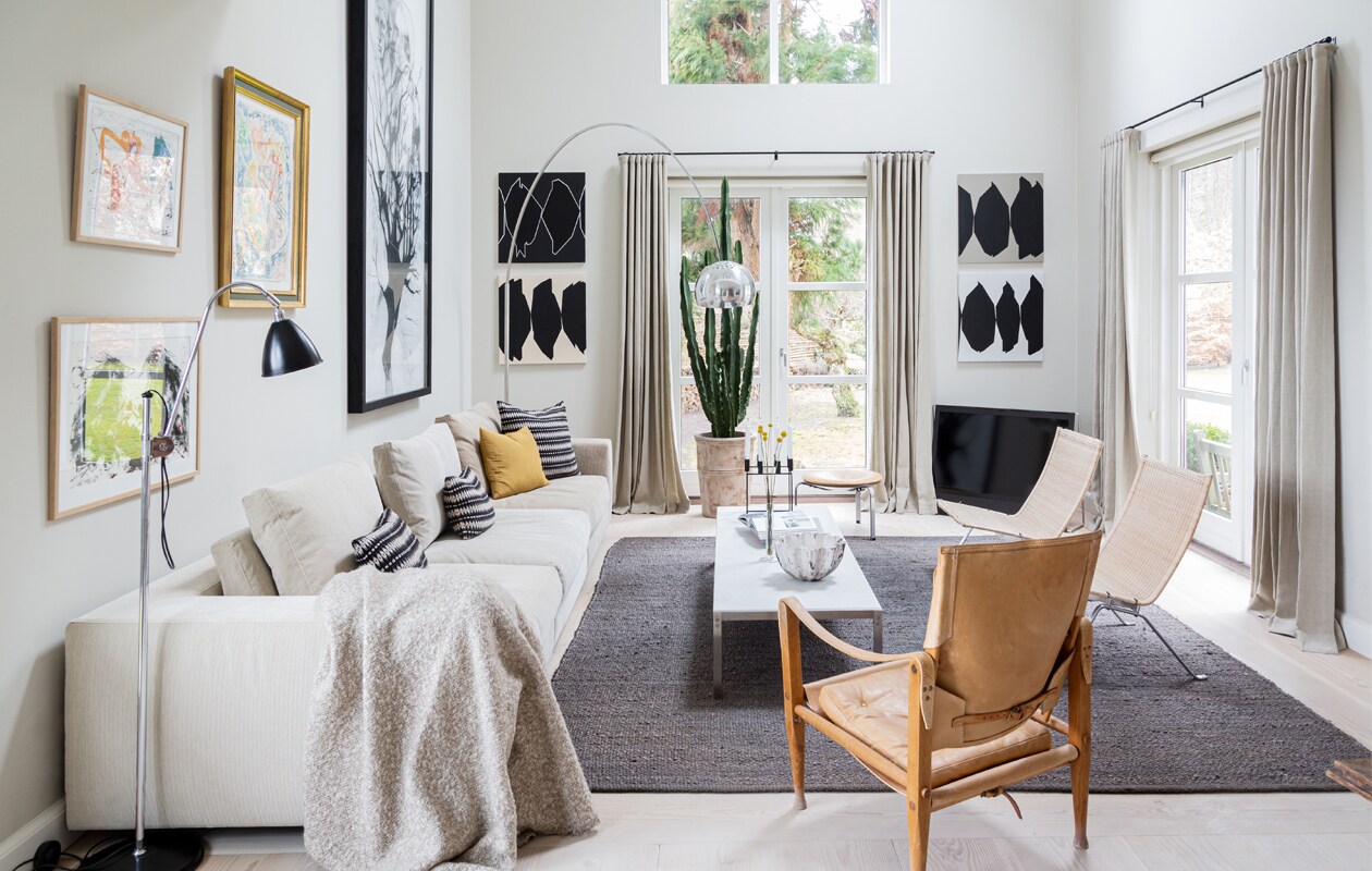 Muurverf Shaded White van Farrow &amp; Ball. Bank Eilersen. Kussens Tapet-Cafe. Koffietafel PK62 en rotan stoelen PK22 van Poul Kjærholm voor Fritz Hansen. Leren stoel Kaare Klint voor Carl Hansen &amp; Son. Vloerlamp Arco van Flos. Schaal gemaakt door een vriendin. Kaarsenstandaard Mogens Lassen. Schilderijen van links naar rechts Carsten Dahl (twee maal), Eigill Jacobsen, Cathrine Raben Davidsen. Grafische kunstwerken Ulla Pedersen. Vloerkleed Tine K Home. vtwonen 13-2020 | Productie Living Inside | Styling Henrietta Sharma | Fotografie Annita Behrendt | Tekst Adeline mans, Pia Olsen