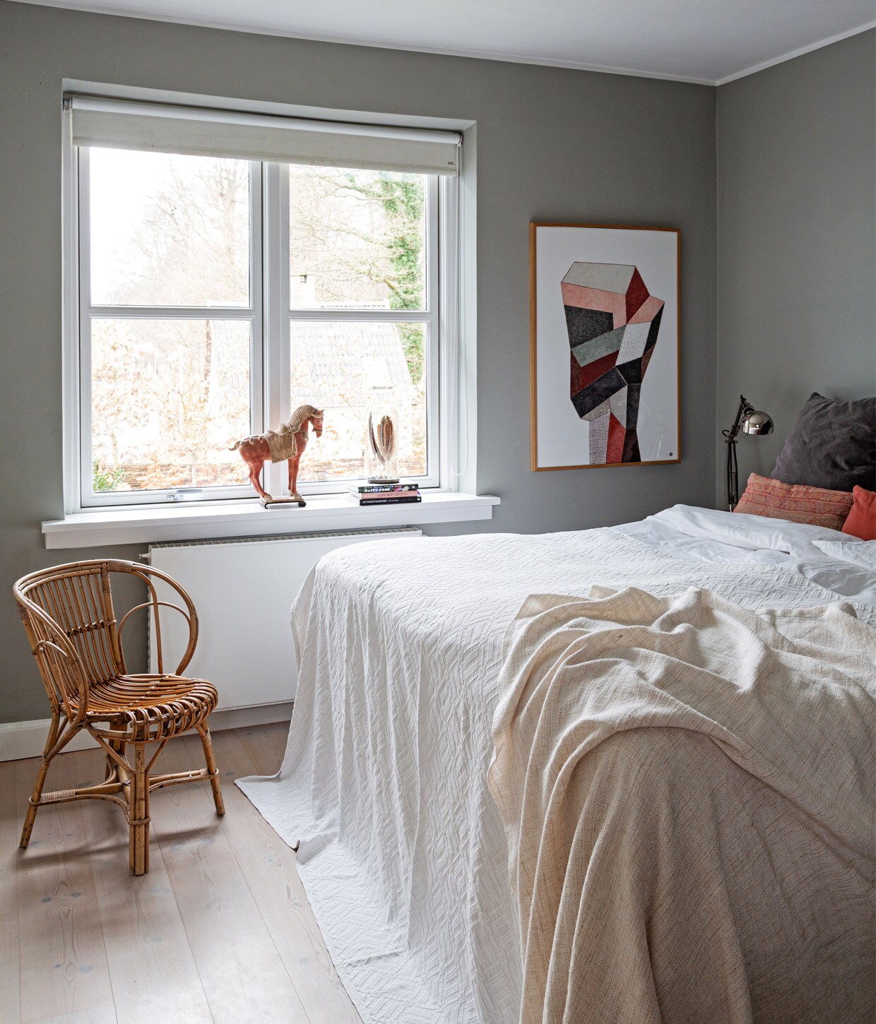 Muurverf Lamp Room Grey van Farrow &amp; Ball. Kunstwerk Nathalie du Pasquir. Houten paard en gevlochten stoel erfstukken. Kussens Studio Oliver Gustav en The Travelling Band. Lakens Ilva. Nachtlamp Ikea. vtwonen 13-2020 | Productie Living Inside | Styling Henrietta Sharma | Fotografie Annita Behrendt | Tekst Adeline mans, Pia Olsen