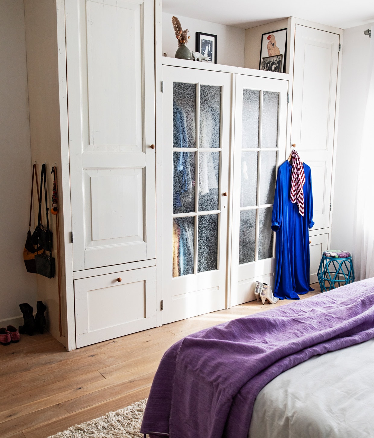 Kast gemaakt met oude deuren uit huis en deuren van Burbri, verf op kast zijdeglans Ral 9010, fotolijsten onbekend, vaas cadeau gekregen, lichtdoorlatende gordijnen vtwonen, blauw krukje vintage, handgemaakte berber pompomdeken The Souks, wit beddengoed Four Leaves, vloerkleed Ikea. vtwonen 12-2020 | Styling Ilona Jongepier | Fotografie Dana van Leeuwen | Tekst Anna van der Heijden