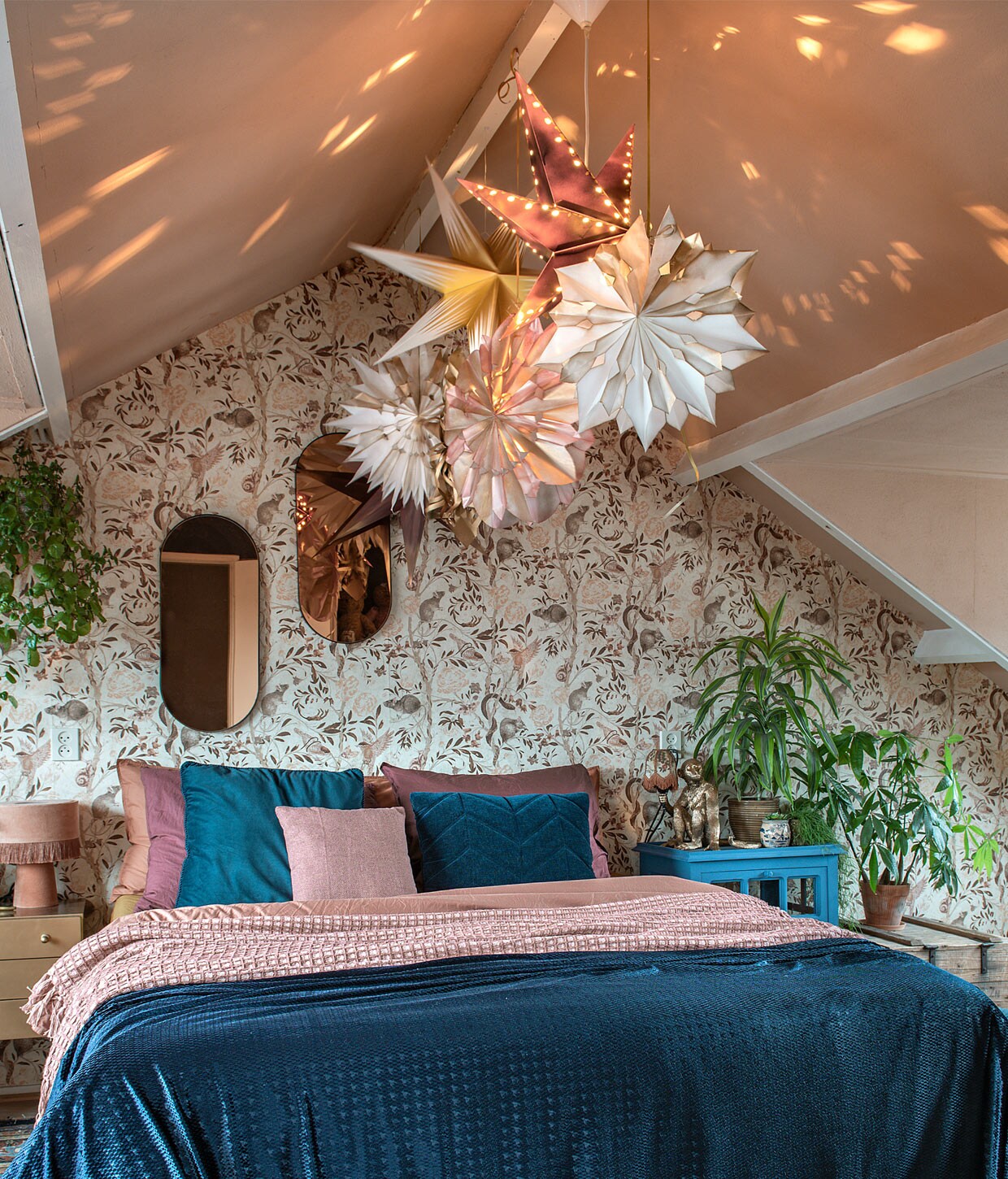 De kerststerren zijn van Ikea en zelfgemaakt met boterhamzakjes. Behang met ratjesdessin Mineheart. Roze plaid en bedlinnen Suite 702. Spiegels en petrol sprei van stof van Kwantum. Kussens: op stoel onbekend, links Boer Staphorst, rechts Volt Studio, klein Jysk. Kastje en stoel kringloop. Lampje Skylerstore. Styling Mindy Schroor | Fotografie Ton Bouwer | Productie en tekst Monique van der Pauw