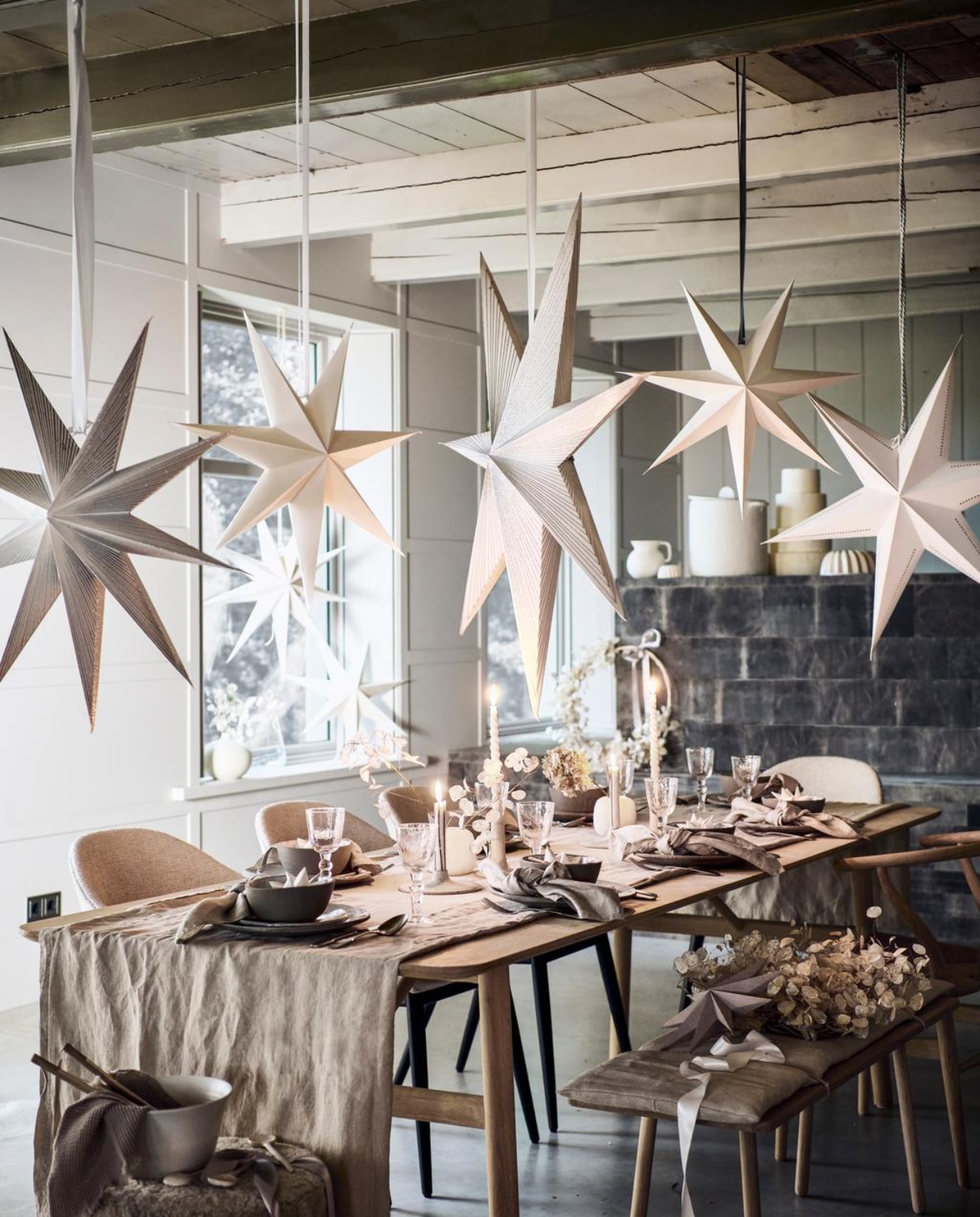 Op en boven tafel: linnen tafelkleed € 39,99, linnen servetten, set van 2 € 9,99, witte papieren kerststerren in kommen, per stuk € 3,99, hangende witte sterren, per stuk € 7,99 (hm.com). Dinerbord per stuk € 37,-, ontbijtbord per stuk € 14,75, kom per stuk € 14,75 (serax.com). Wijnglazen, per stuk € 12,50, stonewashed zilveren bestek, per stuk vanaf € 6,95, witte gedraaide kaarsen, per stuk € 3,50 (paviljoennoord.com). Keramieken kandelaars plat € xxx, hoog € xxx (letoile.store). Albasten vazen, per stuk € 24,99 (sissy-boy.nl). Papieren sterren met zilveren strepen, vanaf € 18,75, witte ster met geperforeerde accenten € 18,75 (bungalow.dk). Interieurontwerp Piet-Jan van den Kommer (vandenkommer.nl). Om de tafel: bouclé kruk van Menu, gestoffeerde eetkamerstoelen van Menu, per stuk € xxx (designtales.nl). Witte schaal van Studio Ro Smit € xxx (factor-ij.amsterdam). Wafeldoek € 7,99 (hm.com). Beige keramieken lepels, per stuk vanaf € 4,99 (sissy-boy.nl). Witte porseleinen lepels, eikenhouten eettafel, houten bank met linnen kussenzitting, houten eetkamerstoel (letoile.store). Grijze papieren ster € 8,- (bungalow.dk). Kransen van judaspenning, vanaf € 39,- (tuinvanjudith.wordpress.com). In de vensterbank en op het aanrecht: keramieken bolvaas € 56,90 (letoile.store). Glazen vaas € 19,99, witte papieren sterren, per stuk € 7,99 (hm.com). Witte keramieken kan € 24,99 (sissy-boy.nl). Tulbandvormen, per stuk vanaf € 11,99 (zarahome.com). Papier-maché pot met deksel € 140,- (paviljoennoord.com). vtwonen 12-2021 | styling Danielle Verheul | fotografie Sjoerd Eickmans | groenstylist Tuin van Judith | assistentie Niels Kist, Kula van den Broek