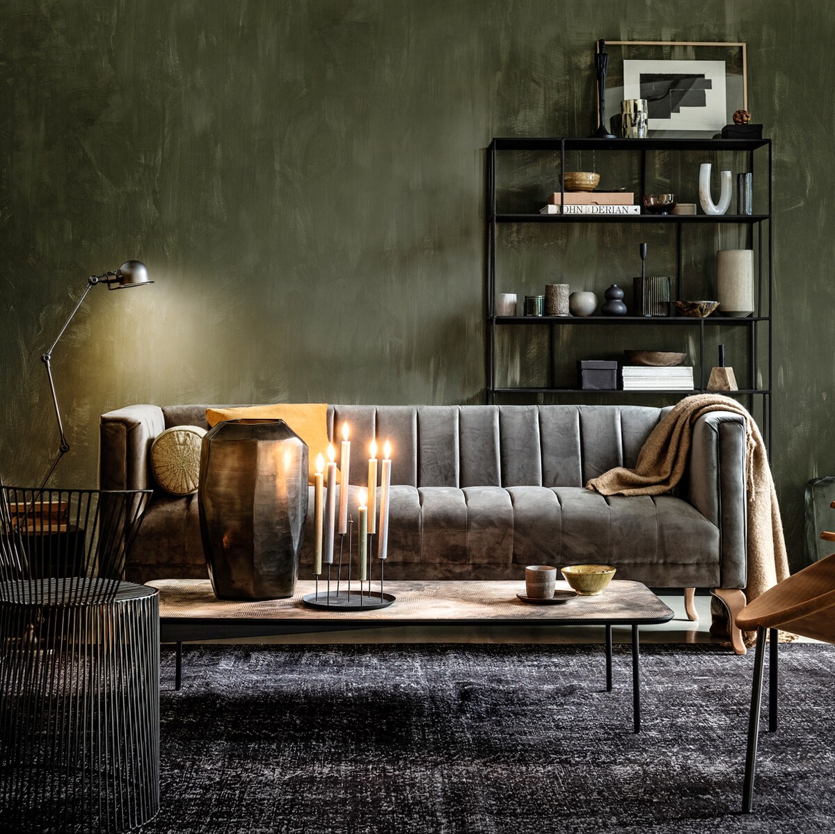 Grijze bank met velours bekleding 205x77x80 cm (bxhxd) (rivieramaison.nl). Verf op wand Fresco kalkverf in kleur Belgian Wilderness, (pure-original.nl). Metalen 4-arm vloerlamp van Jieldé (vdle.nl). Zwarte metalen kast 110x30x180 cm (lxbxh) (polspotten.nl). Groen rolkussen, mosterdgele kom (loods5.nl). Geel velvet kussen, beige wolmix plaid (hm.com). Salontafel, glazen vaas (homestede.nl). Zwarte kandelaar (klevering.nl). Beker, schotel (thingsilike- thingsilove.com). Draadstalen stoel (covanderhorst.nl). Fauteuil met suède zitting (goeds.nl). Zwart vintage vloerkleed 304×172 cm (lxb) (rozenkelim.nl). Kast van boven naar beneden, van links naar rechts: zwart beeld, groene pot met deksel, zwarte metalen kandelaar, bronzen schaal (thingsilikethingsilove). Houten lijst, schaal van hoorn (letoile.store). Zwart-witte waxinelichthouder, mosterdgele kom, witte marmeren kandelaar, marmeren blokkandelaar (loods5.nl). Bruine glazen kom, marmeren pot met deksel, zwart bolvaasje, grijs geribbeld glazen vaas (hm.com). Zachtgrijze vaas (homestede.nl). Overig privébezit. vtwonen 1-2020 | Styling Danielle Verheul | Fotografie Sjoerd Eickmans