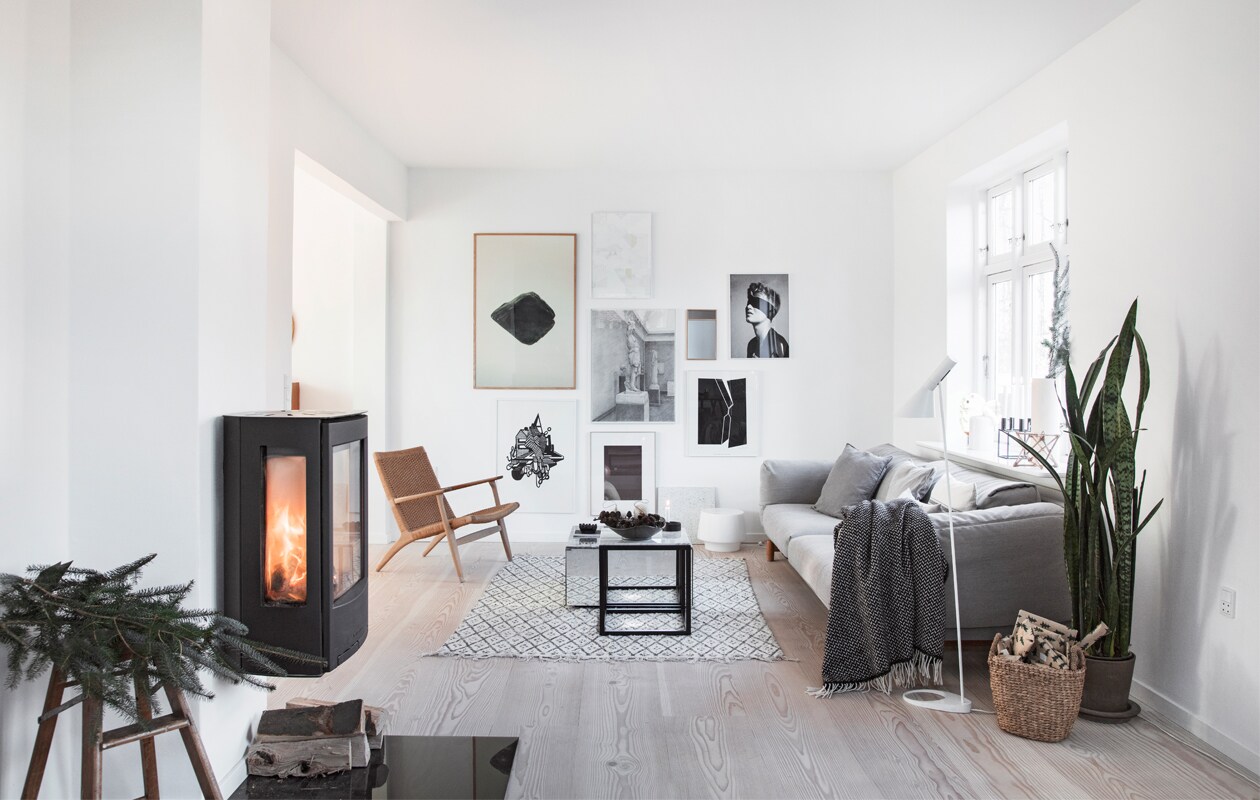 Op de vintage trapkruk dennentakken uit de tuin. Houtkachel Wiking. Bank Muuto. Tafels Kristina Dam Studio. Hans Wegner fauteuil Fritz Hansen. Kleed Nordal. Vloerlamp AJ Louis Poulsen. Plaid Hübsch. Mand Intratuin. Plant Dracaena trifasciata (Vrouwentong) in pot. Kunstwerken mix van zwart-witfoto’s en deels zelfgemaakte illustraties. vtwonen 13-2020 | Styling en tekst Pia Olsen | Fotografie Stine Christiansen | Tekstbewerking Christine van der Hoff