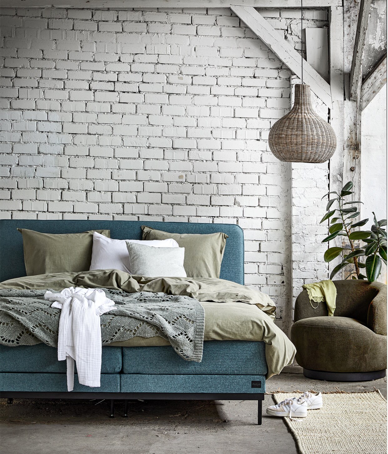 Boxspring Pepper in stof Tweed kleur Moss Green, 180×210 cm vanaf € 2210,-. M.m.v. vtwonen.nl (beddengoed Natural Stone Dark Green en badjas Cuddle van vtwonen), beddinghouse.nl (witte kussensloop, hoeslaken), bepurehome.com (sprei, fauteuil Woolly), bymolle.com (vloerkleed, grijs kussen), adidas.nl (sneakers). couleurlocale.eu (lamp). Overig privébezit.