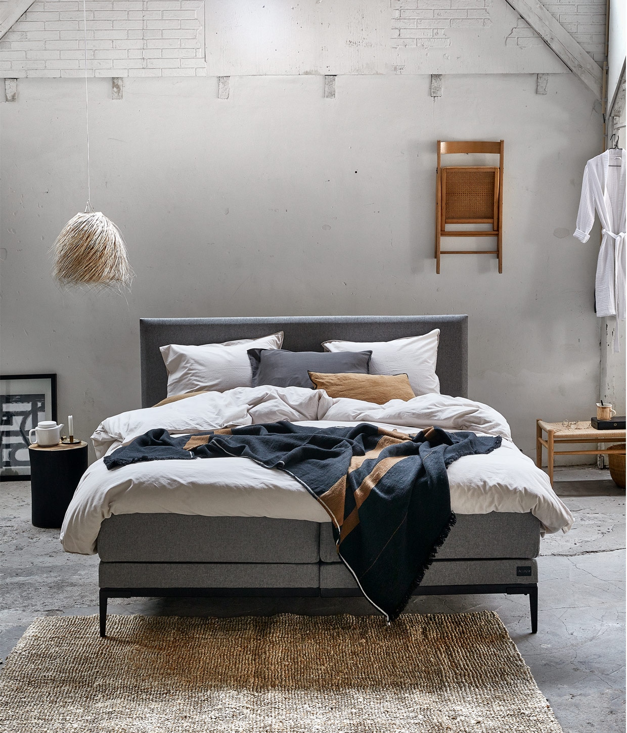 Boxspring Thyme in stof Tweed kleur Middle Grey, 180×210 cm vanaf € 1950,-. M.m.v. vtwonen.nl (dekbedovertrek Natural Stone en kamerjas Cuddle, beide van vtwonen), beddinghouse.nl (kussen in kleur Cinnamon), bymolle.com (bank van Fdb Møbler), couleurlocale.eu (hanglamp, bijzettafel boomstam, plaid, kan), hm.com (vloerkleed), basiclabel.nl (fotolijst met print Blake). Overig privébezit.