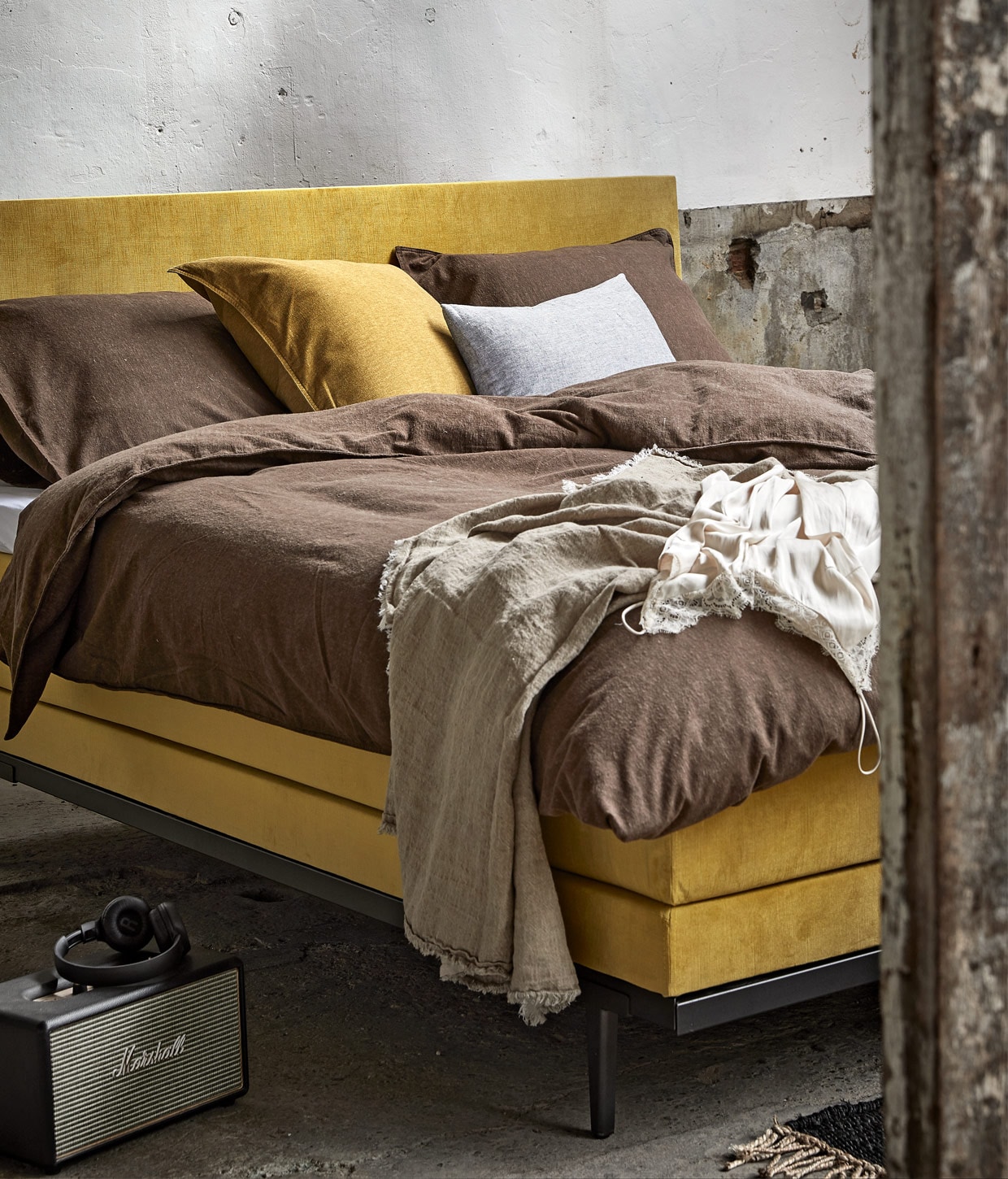 Boxspring Ginger in stof Cube Ocher kleur Yellow, 180×210 cm vanaf € 2150,-. M.m.v. vtwonen.nl (flanellen dekbedovertrek in kleur Earth en okergeel kussensloop, beide van vtwonen), bymolle.com (grijs kussen, plaid), couleurlocale.eu (hanglamp), marshall.com (speaker Acton), basiclabel.nl (print en lijst aan de wand). Overig privébezit.