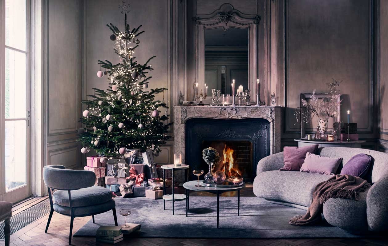 Kerstboom blauwspar (vanvulpenboomkwekerij.nl). Kerstverlichting vanaf € 29,95 (intratuin.nl). Vloerkleed The Moor AP7 in Blue Thunder van &amp;Tradition 200×300 cm € 2060,-, bank Juleo van Taccini in stof Equisetum € 5790,- (kasstoor.nl). Lichtgrijze fauteuil € 2502,- (edha-interieur.nl). Salontafel 77×40 cm (Øxh) € 595,-, bijzettafel met terrazzo-effect blad, 37×55 cm (Øxh) € 285,- (polspotten.nl). Grijze antieke halfronde sidetable, set van 2 € 1250,-, antieke tweearmige kandelaar, prijs op aanvraag, kristallen karaf met oor op salontafel en op de sidetable, vanaf € 60,- (prinsheerlijkantiek.nl). Roze fluwelen kussens, 50×50 cm € 48,- en 60×40 cm € 25,-, paars kussen, Ø 45 cm € 41,-, gedessineerde dozen met deksel, set van 2, vanaf € 45,-, glazen kom op tafel, set van 2 € 30,- (bungalow.dk). Roze cocktailglazen € 10,67, roze glazen karaf € 39,99, roze en okergele kerstballen in fluweellook € 4,-, roze glitterkerstballen € 4,50, gemarmerde roze kerstballen € 4,50, glazen windlicht op bijzettafel € 30,- en op schouw € 40,-, grote glazen kaarsenstandaard € 141,50, roze suède dozen, set van 3 € 106,60 (nordal.eu). Glazen pegelvormige kersthangers € 4,95, gouden vogels € 3,50, gouden vleugels € 3,50, gouden glittersterren vanaf € 12,50, stervormige piek € 12,50, goudkleurige kerstboomhanger € 4,50, glazen ballen met netje vanaf € 4,95, ballen met facetten vanaf € 3,95 (weldaad.com). Antieke zilveren armeluiskandelaars vanaf € 150,- (pietjonker.nl). Plaid € 45,- (maisonnl.com). Keramieken kandelaar € 17,99, goudkleurige kandelaar € 9,99, zilverkleurig dienblad op salontafel € 24,99 (hm.com). Grote glazen lila kerstbal € 9,75 (iblaursen.nl). Wit met goud gedessineerde vaas van Jonathan Adler € 589,- (luxerybynature.nl). Overig privébezit.