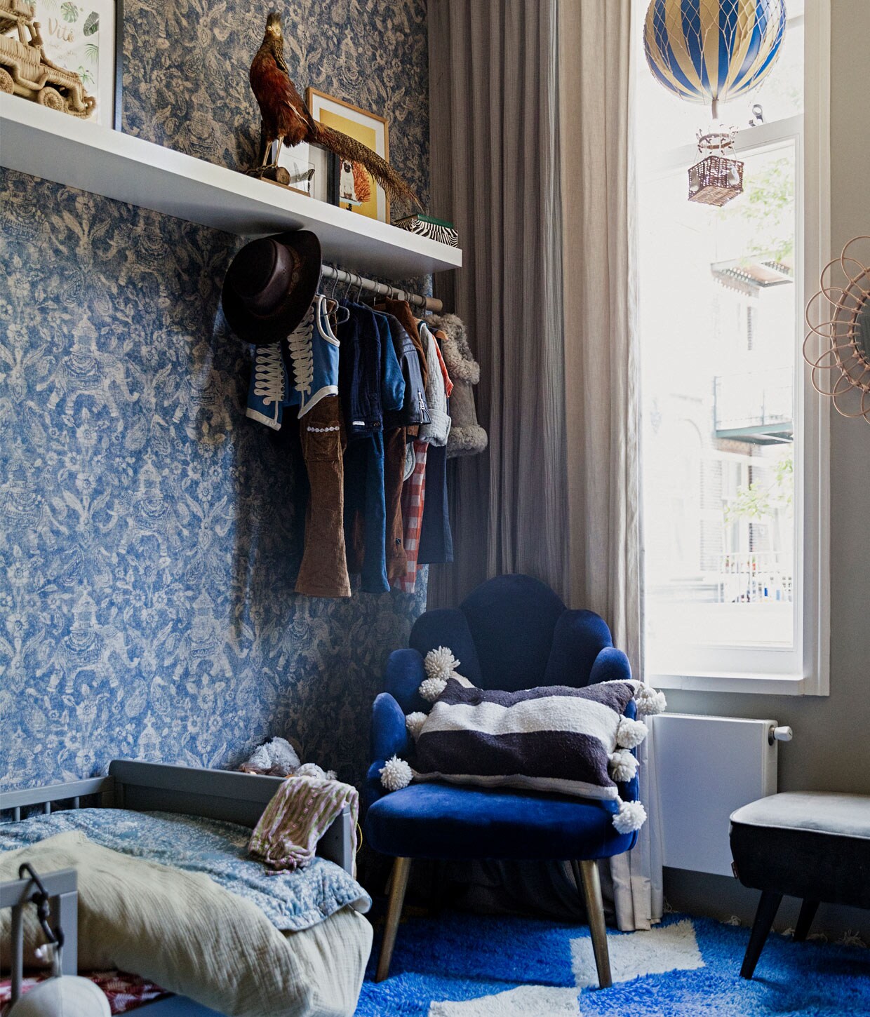 Behang Arte Walls, muurverf French Grey van Farrow &amp; Ball, raambekleding Numero 74, vloerkleed The Weavery, bed Petite Amélie, stoel Sissy-Boy, kussen in stoel The Souks, blauw beddengoed Garbo &amp; Friends, zachtgroen beddengoed Petit Sheets, rood beddengoed onbekend, wandplank Ikea, kunstwerk links naamposter van Fleur des Fleurs, kunstwerk rechts foto van hond Willem door Daan Brand. Opgezette vogel van de rommelmarkt, luchtballon Anna + Nina, spiegel bloem gekregen, bankje Karwei. vtwonen 11-2020 | Productie en styling Ilona Jongepier | Fotografie Dana van Leeuwen | Tekst Anna van der Heijden