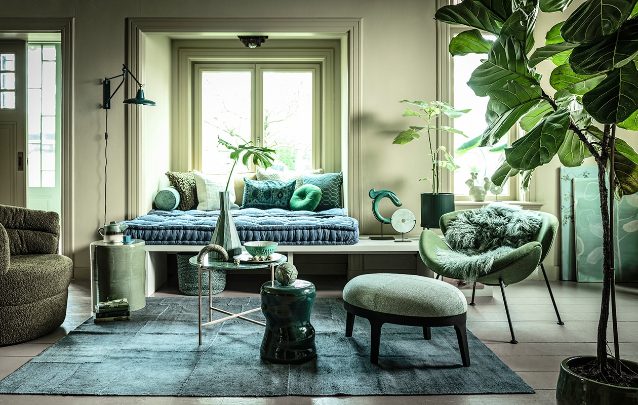 Fauteuil links (flinders.nl). Bank op maat gemaakt (com-anders.nl). Zitting bank twee stuks op maat gemaakt, 210×80 cm, geel/groen langwerpig kussen (coco-mat.com). Fauteuil Orange Slice van Artifort, cactus van Hay (homestede.nl). Marmeren tafel, kruk links, kruk midden, kussen langwerpig met oude opdruk, ronde sierbol op kruk, sierobject draak, vacht, (loods5.nl). Poef, grof kussen, kussen geometrisch (covanderhorst.nl). Marmeren sierobject op tafel (wonenmetlef.nl). Bord, (livingandcompany.com). Theepot (bijenkorf.nl). Vloerkleed, 242×178 cm, langwerpig kussen achter, lichtgroen kussen voor, mand (couleurlocale.eu). Wandlamp Hector van Dutchbone, rond kussen Mandarin van Kaat Amsterdam, Ø 40 cm (vtwonen.nl). Notitieboeken (maisonnl.com). Espressokop en schotel, schaal (ottomania.nl). Rolkussen (hinck.nl). Hoge vaas, ronde siervorm op bank en in vensterbank (badenbaden.nl). Schilderijen achter Branch on a green canvas, 80×100 cm en Floral sketch, original painting, 70×80 cm, (maartjevandennoort.nl). Plantenpot op pootjes (fermliving.com). Plantenpot op grond (uncwardrobe.com).