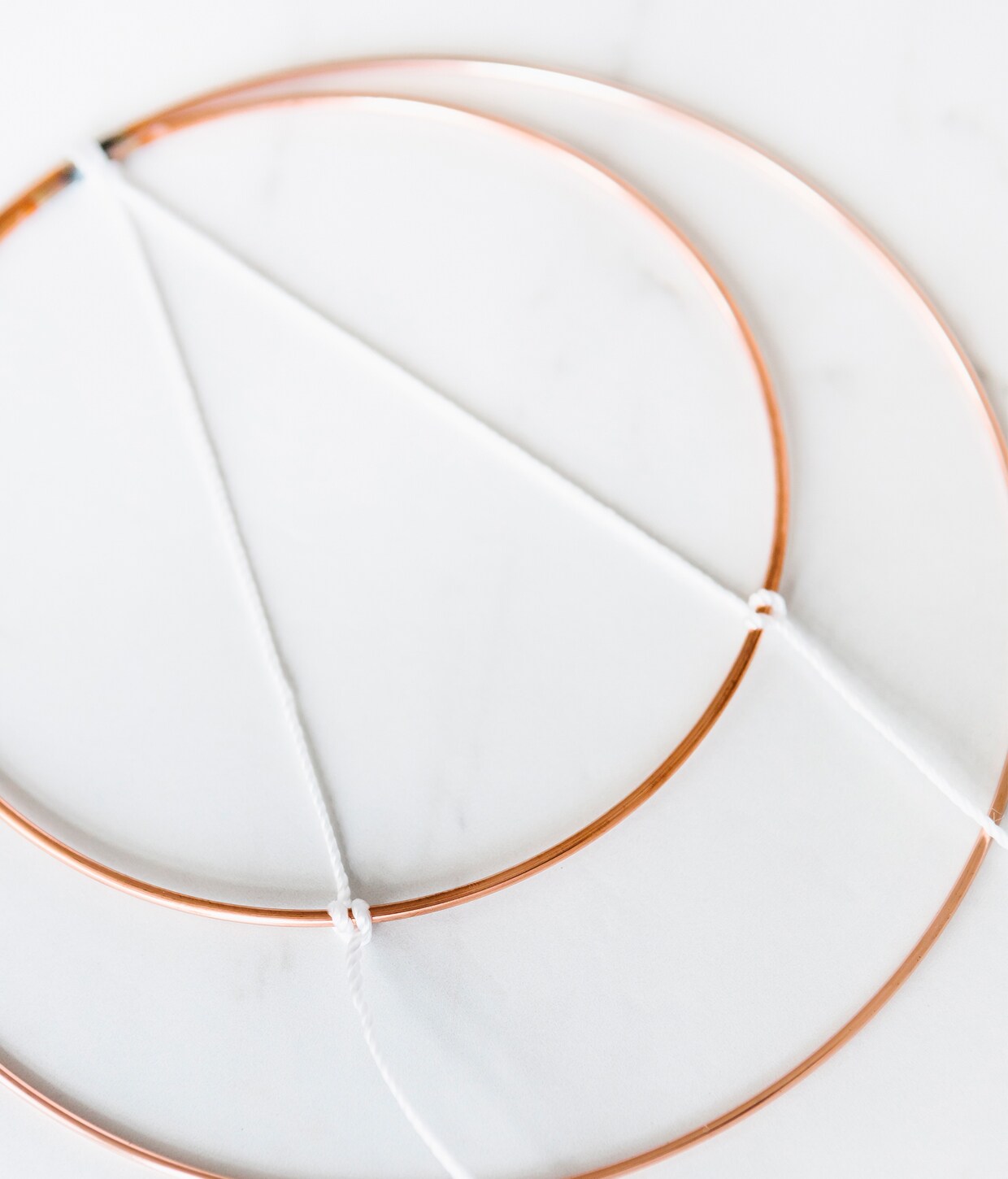 Koperen ring Ø 15 cm € 0,99, koperen ring Ø 20 cm € 1,09, houten kralen Ø 12 mm € 1,69, witte pluimpjes € 2,69, wit koord € 4,49 (ava.be).