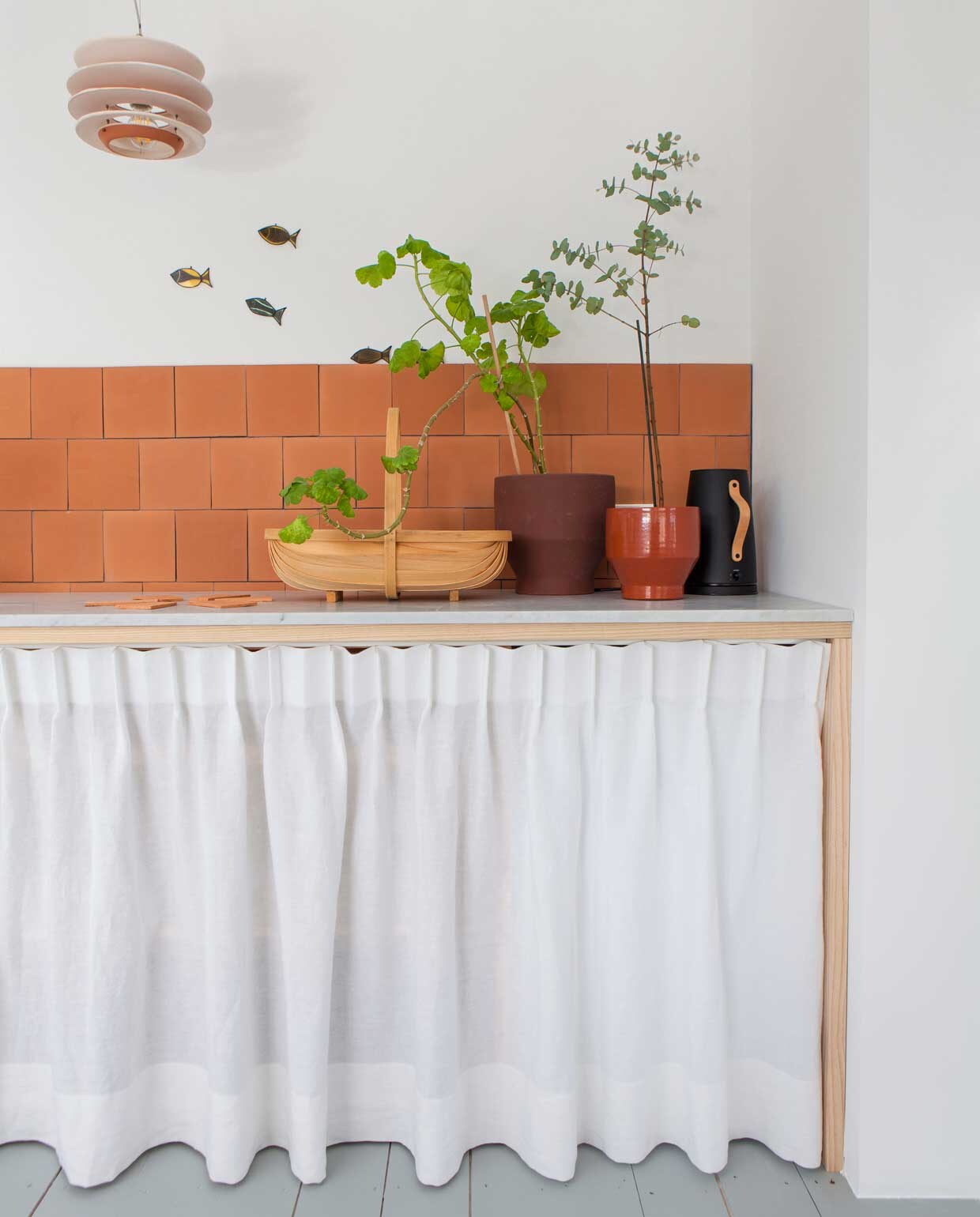 De essenhouten keuken in de studio op de derde verdieping is getimmerd door een meubelmaker. Werkblad en spoelbak van marmer op maat gemaakt. Spatrand betegeld met terracotta tegels van Albarello. Lamp uit Mallorca. Servies Edge van Skagerak. vtwonen binnenkijken special 03-2020 | productie Taverne Agengy | fotografie Anna de Leeuw | Amber van Run