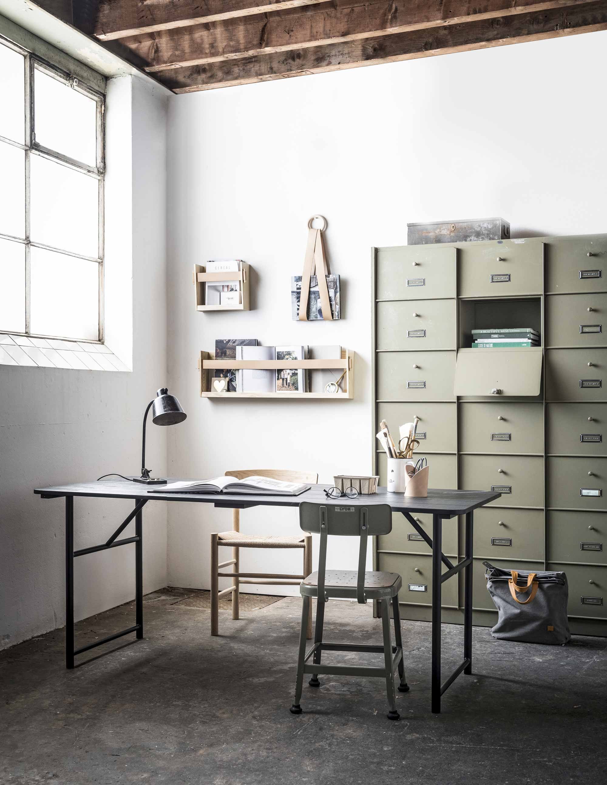 Houten tijdschriftenrek met leren band, leren magazinehouder, leren vaas (Smålands Skinnmanufaktur). Metalen klepkast (Van Dijk &amp; Ko). Metalen kist (De Weldaad). Stapel boeken in de klepkast, boek op tafel (Loft). Houten stoel J39 (Pantoufle). Army eettafel zwart met ijzeren poot (vtwonen.nl). Zwarte bureaulamp (Neef Louis). Metalen stoel (lyonbarstools.com). Boek Home (vtwonen.nl). Grijze tas, kartonnen doosje, bril, pot met kwasten privébezit.