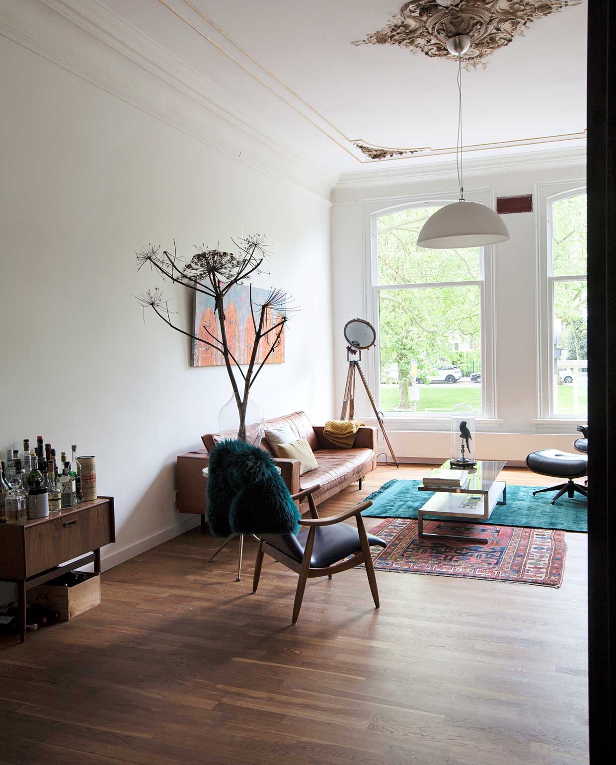 Vintage drankenkabinet, houten stoel met blauwe bekleding en salontafel Bestwelhip. Groene vacht en bijzettafel met driepoot Kieveen. Bruine bank Albufera van Lederland, kussens de Bijenkorf, gele plaid De Groene Lantaarn. Schilderij boven de bank van Merijn Kavelaars. Staande lamp 360Volt. Turquoise kleed Kieveen, Perzisch kleed van oma. Glazen stolp met vogel herkomst onbekend. vtwonen binnenkijken special 12-2020 | Fotografie Corine Hoge Bavel | Styling Sheila Sletbeen via Kieveen