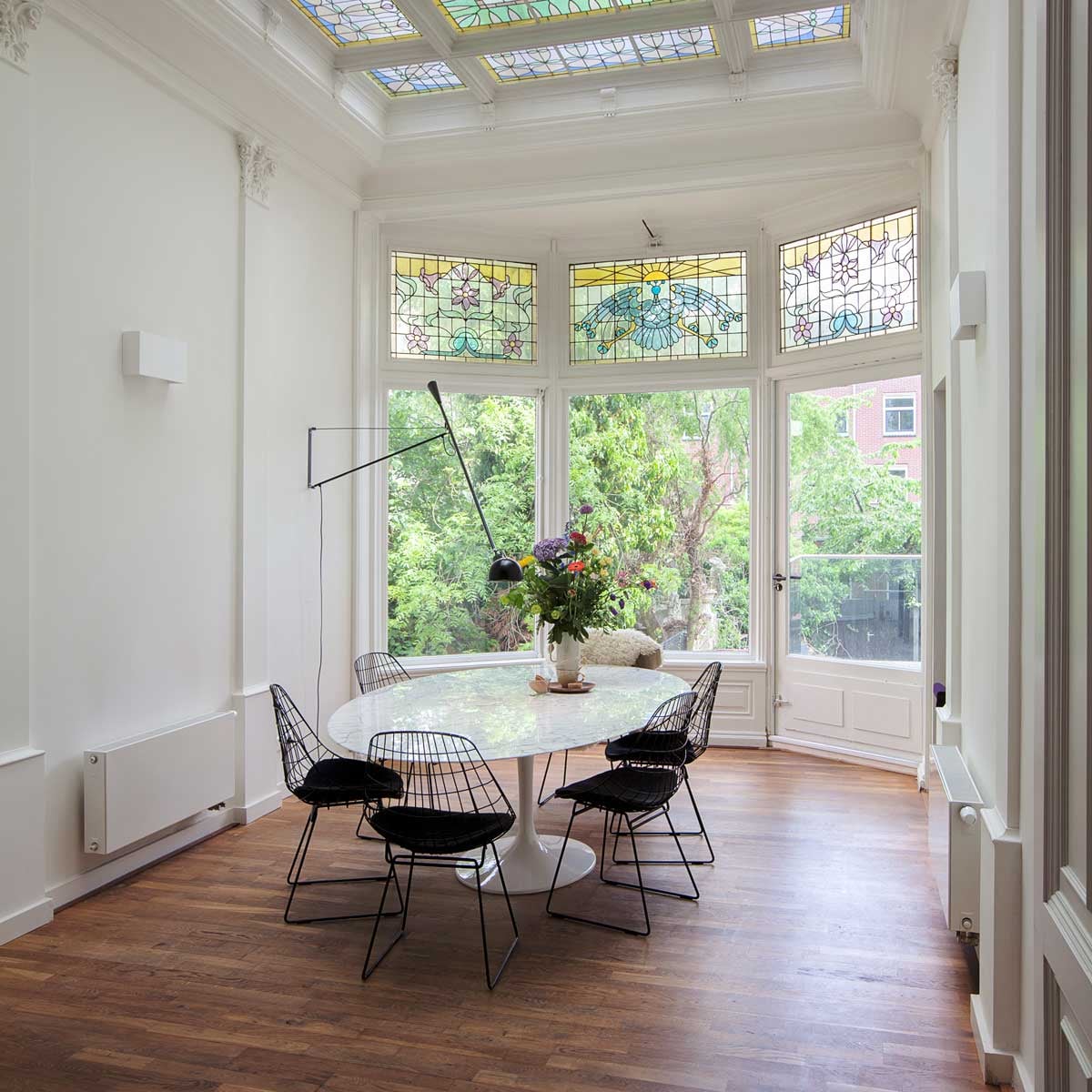 Tafel met marmeren blad van Eero Saarinen voor Knoll, draadstalen stoelen SM05 van Cees Braakman voor Pastoe, vacht van de biologische Nieuwmarkt in Amsterdam. Wandlamp 265 van Flos. Vaas herkomst onbekend. Kop en schotels Kieveen. Muurschildering in doorgang gemaakt door Merijn Kavelaars. vtwonen binnenkijken special 12-2020 | fotografie Corine Hoge Bavel | styling Sheila Sletbeen via Kieveen