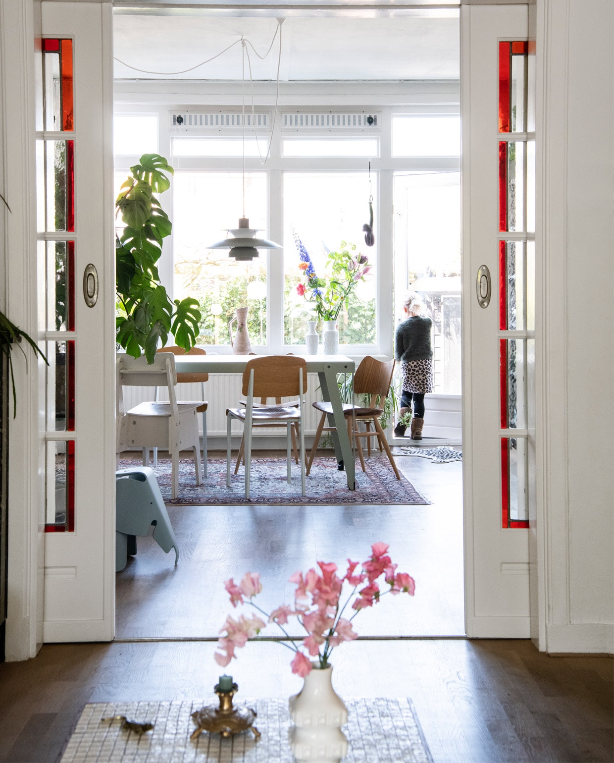 Tafel Lloyd van Functionals. Vloerkleed erfstuk van Kims opa en oma, hanglampen PH5 van Louis Poulson. Vintage houten stoelen. Witte stoelen Piet Hein Eek. Witte kinderstoel Ikea. Foto in Argentinië gemaakt door Bart. Vintage plantentafel Sprinkel + Hop. Plantenpotten vintage, onder andere van Fortune Flea. Gordijnen Ikea. Bloemen Tof Amstelveen. Kaketoe op tafel &amp;klevering. vtwonen binnenkijk special 12-2020 | productie Insidehomepage | styling Kim Timmerman | fotografie Louis Lemaire