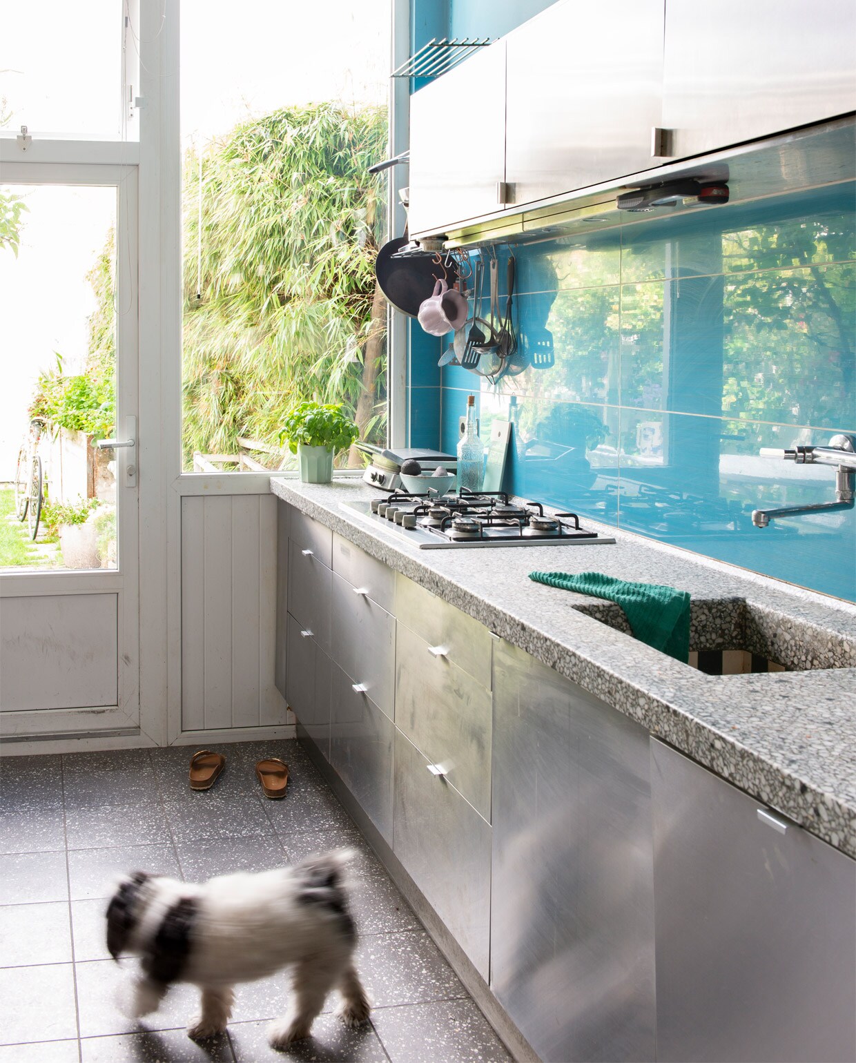 RVS keuken Ikea, handgemaakt granieten blad van F. Cristofoli, tegels Jan Groen. Muurverf IG025-E van Gamma. Herkomst bloempot en schaal onbekend, lila kan Mynte van IB Laursen, blauwe kan Kitsch Kitchen.