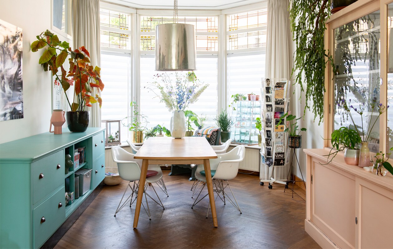 Dressoir en roze buffetkast Van Dijk &amp; Ko, blauwe schoolbordverf GN-039-10 van Gamma. Roze vaas Return to Sender, plantenpot Intratuin. Hanglamp en tafel Loods 5. Stoelen Eames DAR van Vitra. Witte vaas Pols Potten. Kaartenrek vintage. Kunstwerk Nienke Sybrandy. Plantenstandaard Ferm Living
