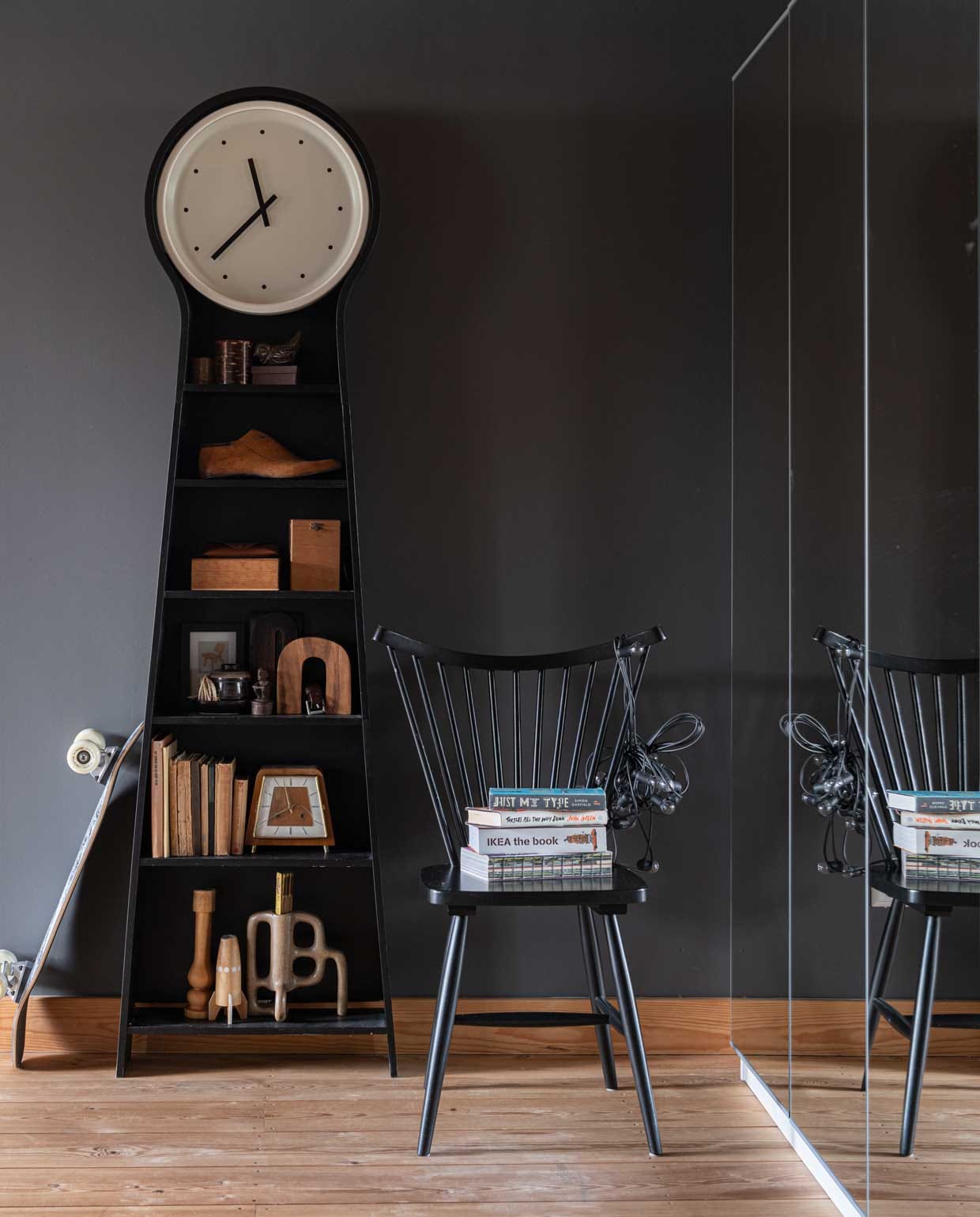Grootvaderklok uit de Ikea PS collectie. Daarin collectie met ambachtelijke en vintage voorwerpen, antieke boeken. Raketvormige kandelaar Bolia, kandelaar rechts uit Kioto, stoel en spiegelkast Ikea. Muurverf Industrial Grey van Flexa. vtwonen binnenkijkspecial 12-2020 | styling Sharon Roest | fotografie Caroline Martinot