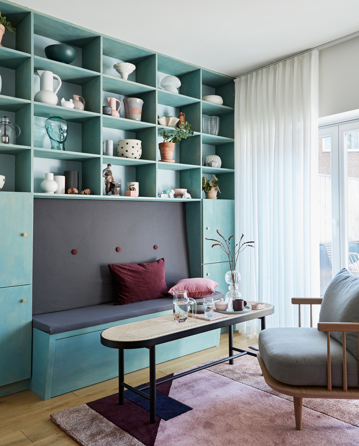 De vakkenkast met ingebouwde bank is geverfd met lijnolieverf in kleur Havgrøn (Ocean Green) van Nature Paint. Deze verf kleurt het hout, terwijl het transparant is, zodat de structuur van het hout zichtbaar blijft. Muur geschilderd in kleur Risør 4120 van Jotun. Salontafel van Warm Nordic, stoel van &amp;Tradition, kleed van Please Wait to be Seated.