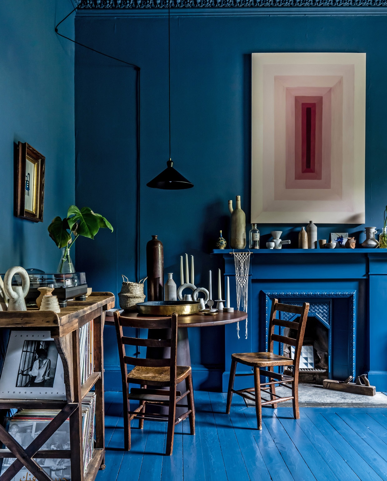 Verf op vloer, wanden en plafond Hague Blue van Farrow &amp; Ball. Een hergebruikte fabriekswerkbank dient als platenrek. Tafel ontworpen door Tokes en door een lokale timmerman gemaakt van oude werkbladen uit scheikundelokalen. Stoelen uit een kerk. Geometrische schilderij en aardewerk op de schouw gemaakt door Tokes.