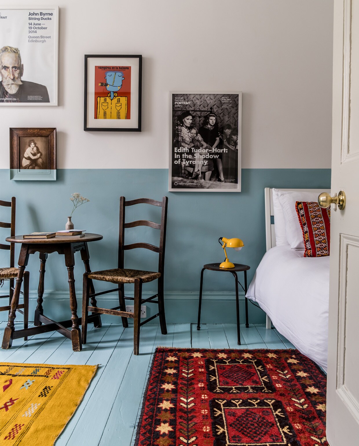 Een van de twee logeerkamers, te huur via Airbnb. Verf op vloer en wand Blue Ground van Farrow &amp; Ball. Vloerkleden souvenirs uit Marokko. Ronde tafel uit een kroeg, antieke stoel uit een kerk. Kruk van Arne Jacobsen en lampen vintage vondsten. Schilderij gemaakt door Tokes.