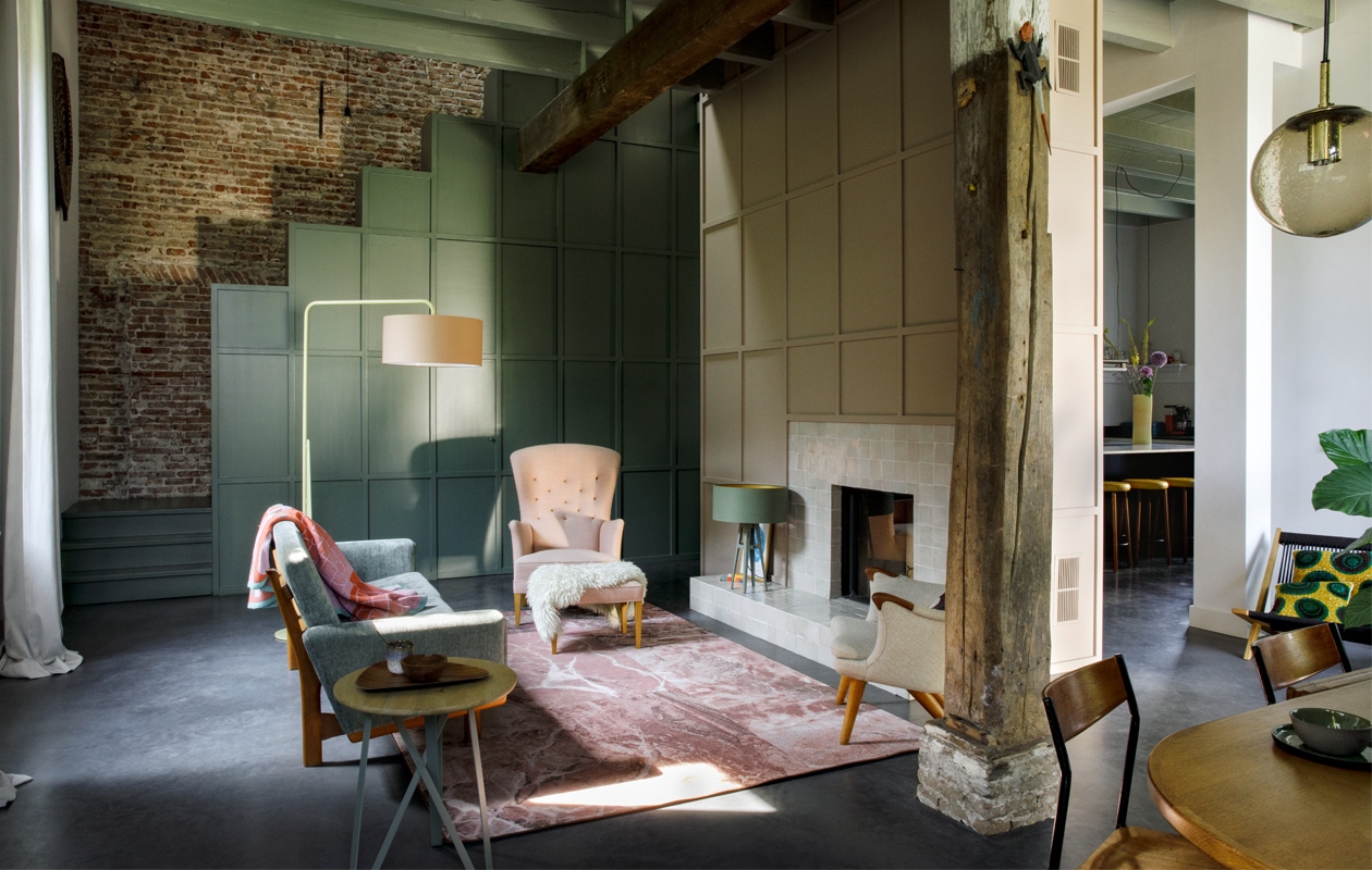Gordijnen, vakken bij trap en vlakverdeling boven de haard eigen ontwerp. Verfkleur trap en trapkast Green Smoke, Farrow &amp; Ball. Tegels haard Rozetta. Vintage bank, fauteuils en voetenbank Morentz, plaid Sigrid Calon. Vloerkleed Sense of Marble van Desso. Lampen en bijzettafel Twister van Spoinq. Dienblad en kop herkomst onbekend. Schaal en schapenvacht lokale markt.  vtwonen 10-2020 | fotografie Inga Powilleit | styling José Martens