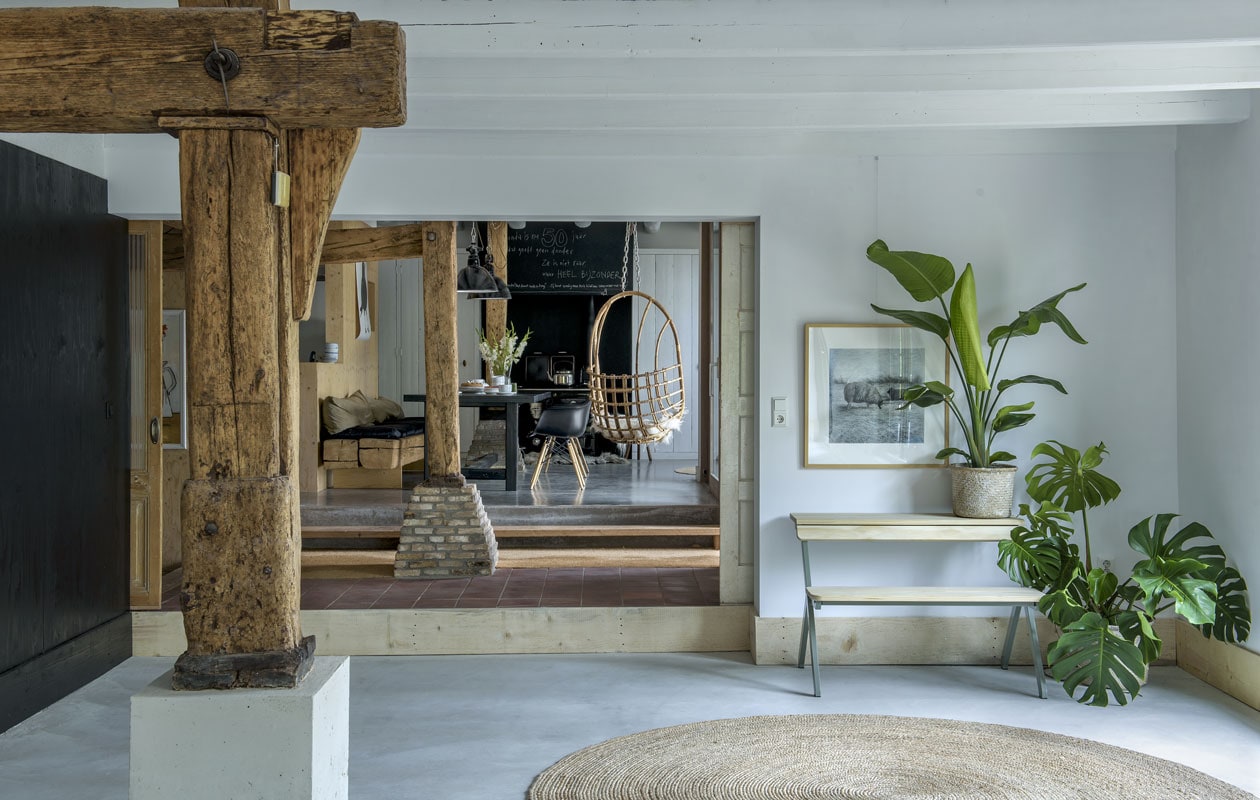 De tafel en het bankje werden zelfgemaakt van materialen uit het huis. De zwarte stoelen zijn van Eames. Lampen van Buitengewoon Brocante. De kruk was van Dietriks vader. Illustratie Maartje van den Noort. De oude staander loopt door tot aan het dak. De vloer is van beton.
