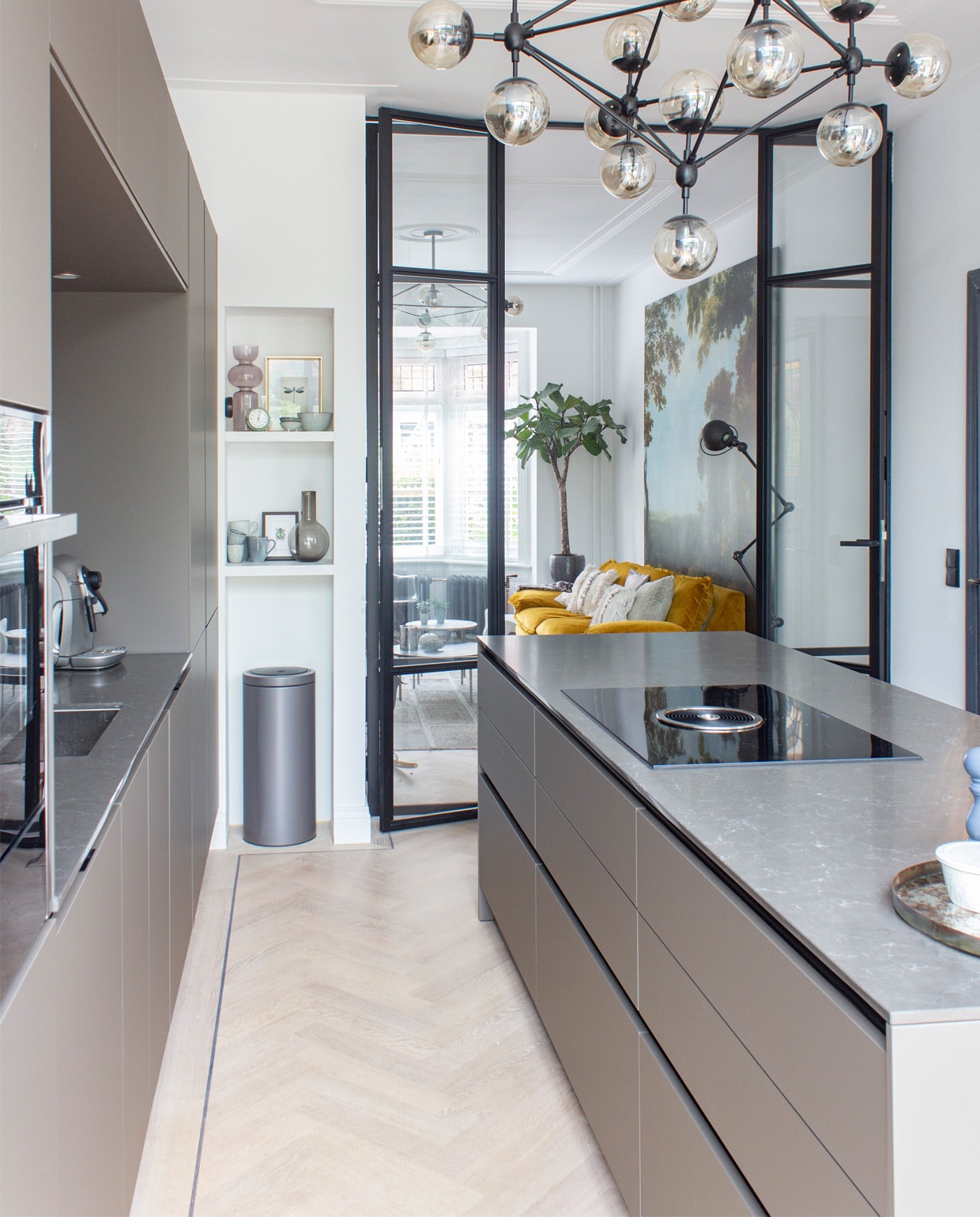 Siematic-keuken in kleur Umbra in matte uitvoering met een blad van composiet. Lamp met rookglas Loftlamp. In de nis: bruine vaas Karwei, bruine karaf H&amp;M home, mokken van Broste Copenhagen. De stalen binnenpui is gemaakt door Brink Stalen Deuren. Prullenbak Brabantia. vtwonen special 03-2020 | styling Angela Zonneveld, Decorush | fotografie Anne Kohnke