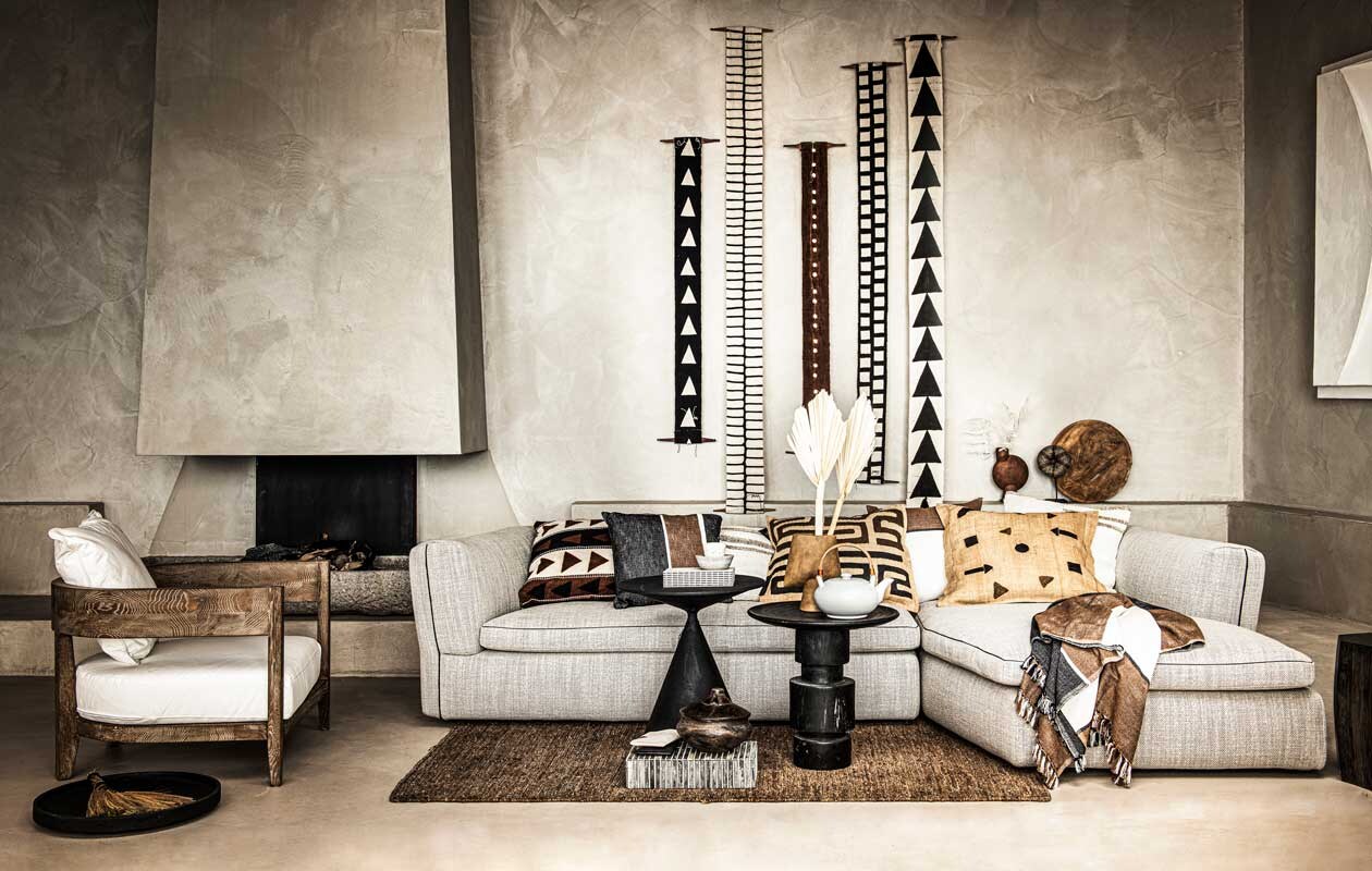 Loungestoel met houten frame € 950,- (nettydegroot.nl). Schaal op de grond € 95,-, bijzettafel links € 1799,-, vaas op bijzettafel rechts € 50,-, bruine vaas achteraan € 40,-, hoekbank € 11.330,- (edha-interieur.nl). Totem wandhanger vanaf € 79,-, kussen links op de bank € 199,-, theepot € 79,-, zwart en wit mapje op doos, per stuk € 22,-, wit kopje op tafel € 25,-, schaaltje op tafel € 30,-, boek € 65,- (sukha.nl). Kussen tweede van links, 50×50 cm € 39,95, kussen in het midden met zwarte tekening Unique Pieces vanaf € 220,-, kussen rechts ernaast 50×50 cm € 39,95, kussen met pijlen en stippen Unique Pieces vanaf € 220,-, plaid op de bank 130×200 cm € 129,95 (mlfabrics.nl). Kwast op schaal € 25,99 (zarahome.com). Doos op de grond € 247,11 (badenbaden.nl). Droogtakken prijs op aanvraag (waterdrinker.nl). Houten schaal tegen achterwand € 79,-, ecru kelimkussen met beige streep uit Turkije, 50×50 cm per stuk € 49,- (couleurlocale.eu). Houten ronde pot op de grond € 95,-, kralen armband op statief op achtergrond € 109,- (o-live.nl). Overig bezit van de locatie (republiekbloemendaal.nl). Beeld: vtwonen 9-2020 | styling Liza Wassenaar | fotografie Sjoerd Eickmans | assistent Thomas van der mark | locatie republiekbloemendaal