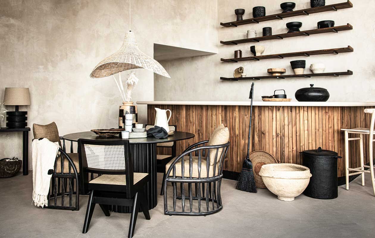 Ronde tafel Ø 140 cm € 895,- (hklving.nl). Over de stoel katoenen plaid Woood Esmee 130×170 cm € 19,95, op tafel: zwart servet Broste Copenhagen Gracie 45×45 cm , € 9,40, roomwitte kopjes Serax Merci per stuk € 8,95, bruine borden Leonardo per stuk , € 12,95,-, houten lepels in schaal Serax Pure 5-delige set € 53, roomwitte borden Serax Merci 23×15 cm per stuk € 11,10, theepot op bar Serax Collage 1,2 l € 89,- (vtwonen.nl). Op de planken: mand half zwart, half beige pedestal 30×25 cm € 69,-, soortgelijke mand horizontaal gestreept 31×32 cm € 69,-, op bar houten schaal € 79,-, op tafel geblokte terracotta vaas Pot Damier € 145,-, hanglamp ijzer en riet € 336,- (couleurlocale.eu). Zwarte stoel met rotan per stuk € 1595,- (edha-interieur.nl). Witte keramieken vaas links net in beeld € 50,-, rond bakje op tafel € 30,- (sukha.nl). Plaid in mand links op grond 130×200 cm € 129,95 (mlfabrics.nl). Droogtakken, prijs op aanvraag (waterdrinker.nl). Gevlochten mand links op tafel € 109,-, kralenarmband op onderste plank op statief € 109,- (o-live.nl). Witte kan op tafel € 35,99, gevlochten mand tegen de bar € 22,99, keramieken schaal onderste plank € 45,99, roomwit potje onderste plank links € 9,99, wijnkoeler tweede plank van onder links € 35,99 (zarahome.com). Zwarte grote mand Serax € 225,- (nettydegroot.nl). Grote witte mand € 47,50 (aurapeeperkorn.com). Overig privébezit of bezit van de locatie (republiekbloemendaal.nl).