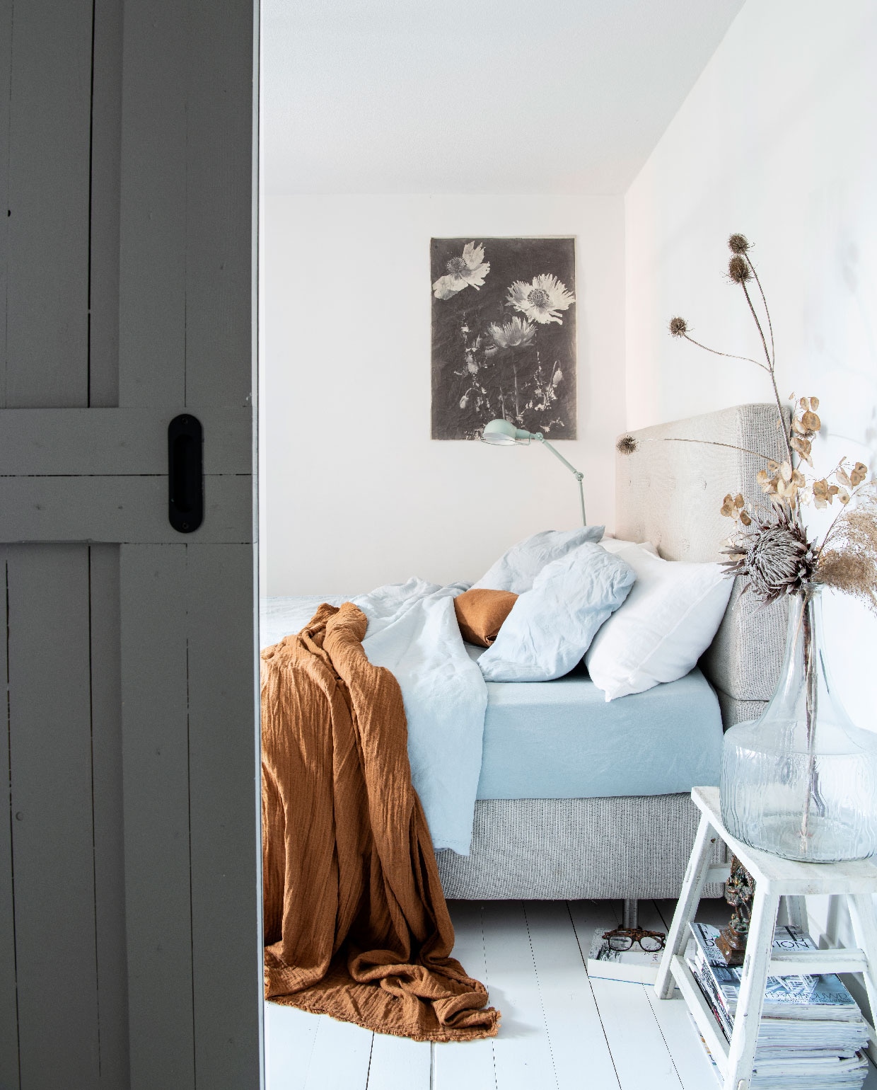 Houten vloer Pont Meyer Zaandam. Botanische print aan de muur Mo-ca. Bed Ikea. Lamp Made. Blauw beddengoed Dutch Home Fabrics. Plaid H&amp;M Home. Kruk tweedehands. Vaas op kruk Zuiver. Schuifdeuren gemaakt door aannemer. vtwonen 09-2020 | productie Insidehomepage | fotografie Louis Lemaire | styling Marit Saladini