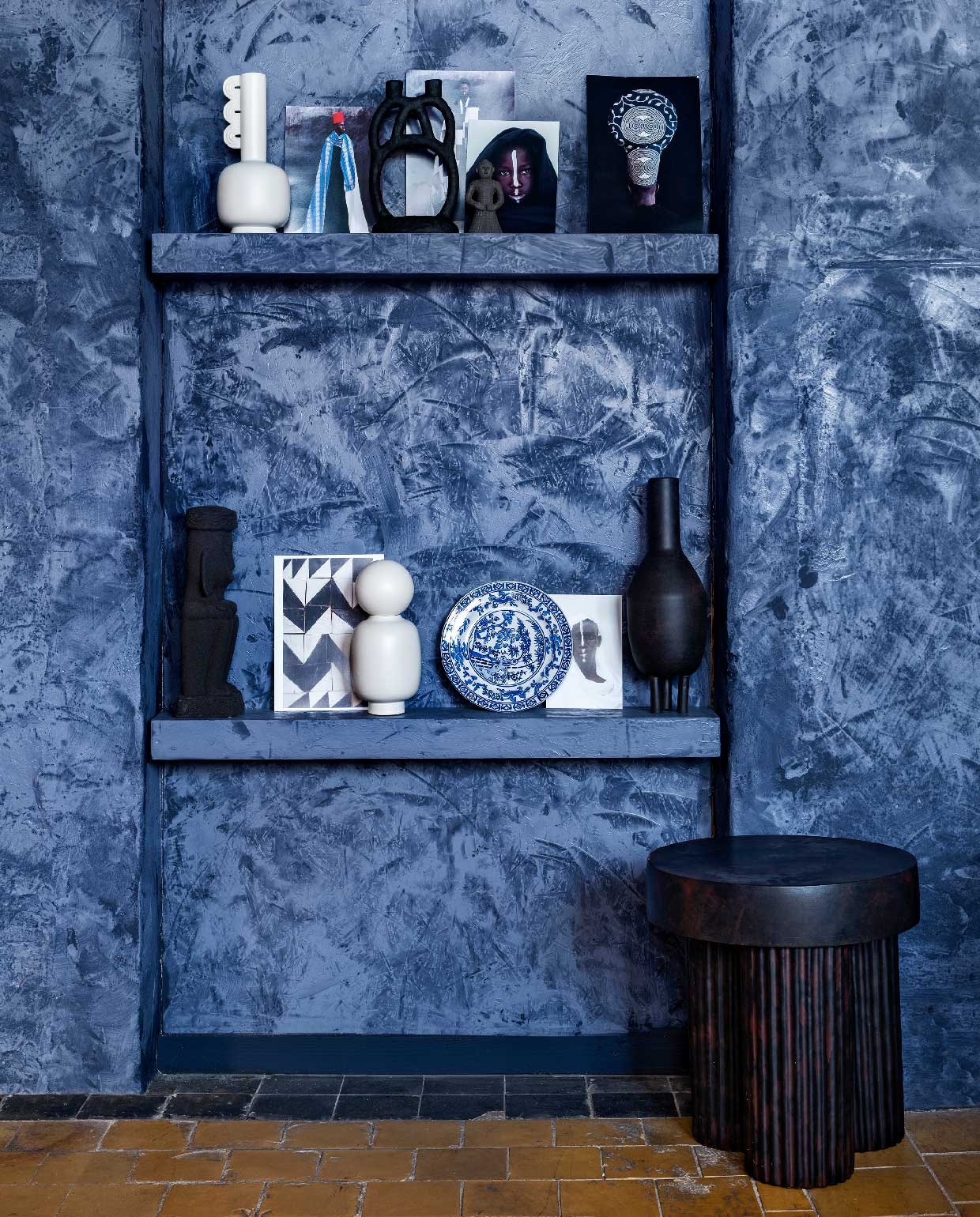 Op de muur krijtverf Majestic Cloth met verftechniek Marrakesh Walls per liter € 111,25 (pure-original.nl). Tafel Gear maat High € 349,- (norr11.com). Kandelaar van House Doctor € 39,90 (vtwonen.nl). Witte vazen van Ferm Living vanaf € 79,- (eijerkamp.nl). Blauw-wit bord € 13,95 (hkliving.nl). Incabeeld klein € 6,25 en groot € 34,50 van Madam Stoltz (deens.nl). Zwarte vaas op driepoot € 99,- (101cph.com). Portretten uit boek Inner Constellations van Maimouna Guerresi (amazon.com).