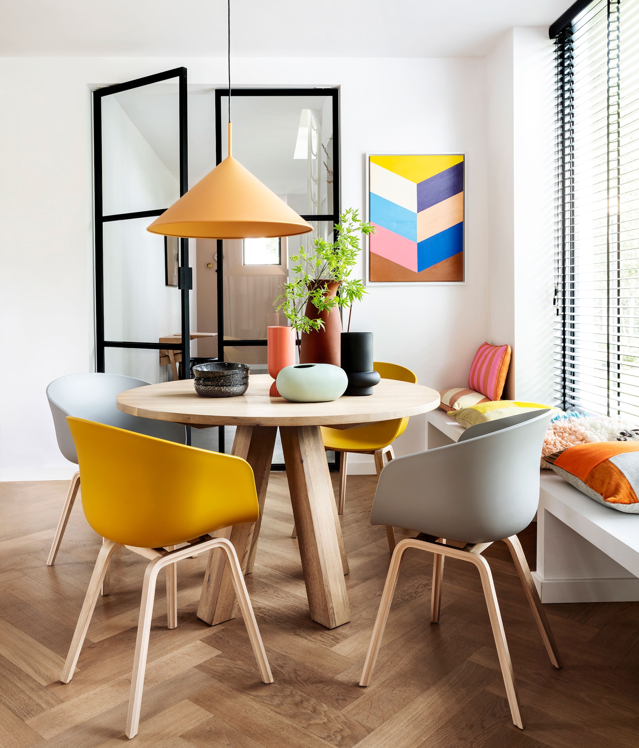 Eettafel Alaska, 120×78 cm (Øxh) € 1095,-,  (hetkabinet.nl). Eetkamerstoelen About,  a Chair van Hay in Mustard en Concrete,  Grey per stuk € 249,- (vtwonen.nl).,  Hanglamp Triangle, 60×39 cm (Øxh),  € 239,-, schilderij Colourful Strokes,  € 139,95, oranje-roze gestreept kussen,  € 47,95, perzik-crème gestreept kussen,  € 34,95, koraalrode vaas Suites Special,  € 27,95 (hkliving.nl). Wollen kussen,  Multi € 39,95, zwarte vaas Corsica,  € 17,50, borden Odile per stuk € 10,-,,  ovale mintkleurige vaas € 16,95,  (loods5.nl). Kussen met oranje vlakken,  € 115,- (kus-sen.nl). Overig privébezit.