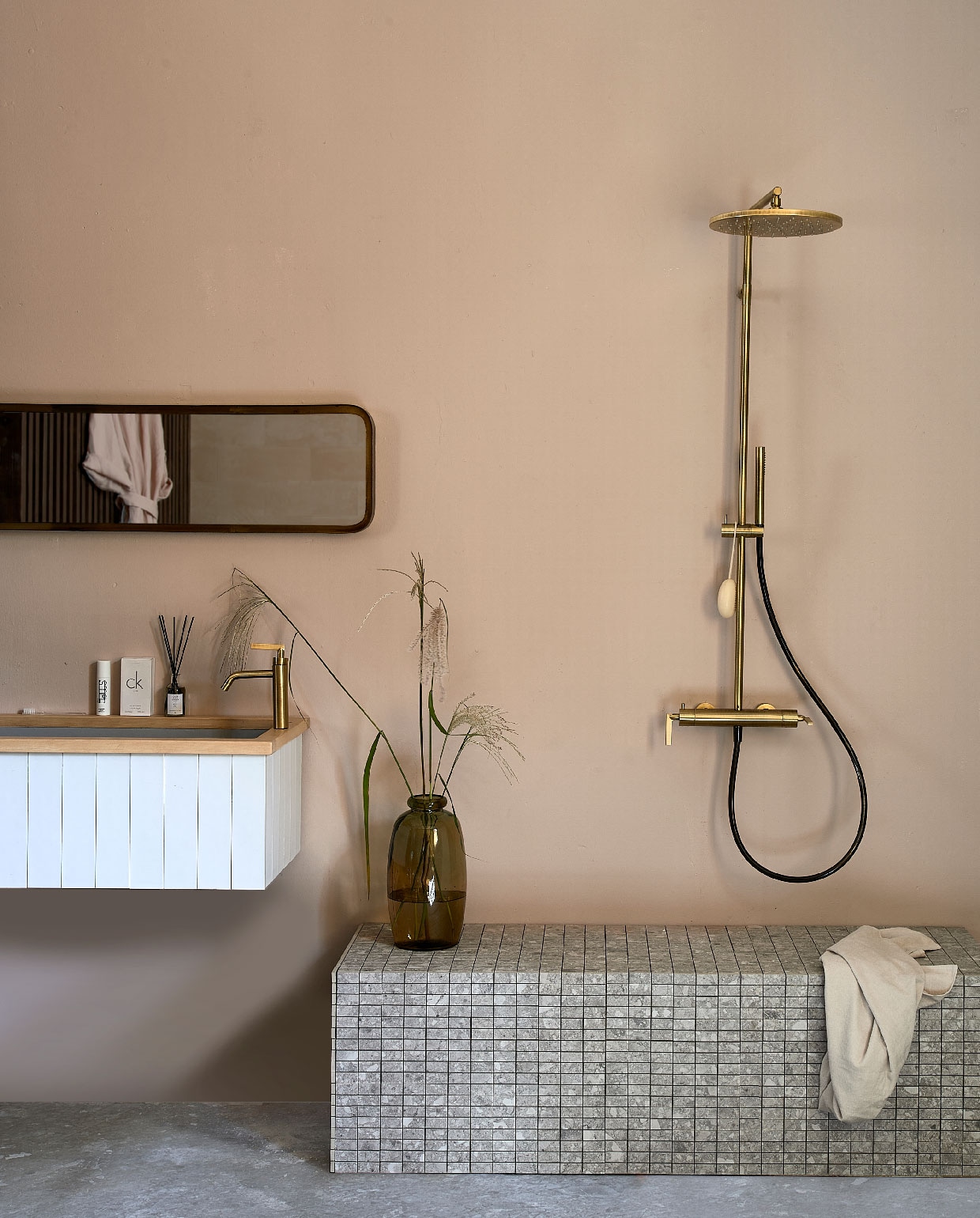 Wastafel op maat gemaakt en betegeld met wandtegel Mediterranea Calpe Blanco van vtwonen, 7,5×30 cm € 78,85 per m², Composite Mozaiek Light Grey van vtwonen, 30×30 cm € 26,00 per stuk. (vtwonentegels.nl). Douchekraancombinatie Grip in Bronze van vtwonen € 2188,- (vtwonen.nl). Spiegel € 149,- (basiclabel.nl). Handdoek € 8,99 (hm.com). Bruine vaas € 25,- (loods5.nl). Overig privébezit.