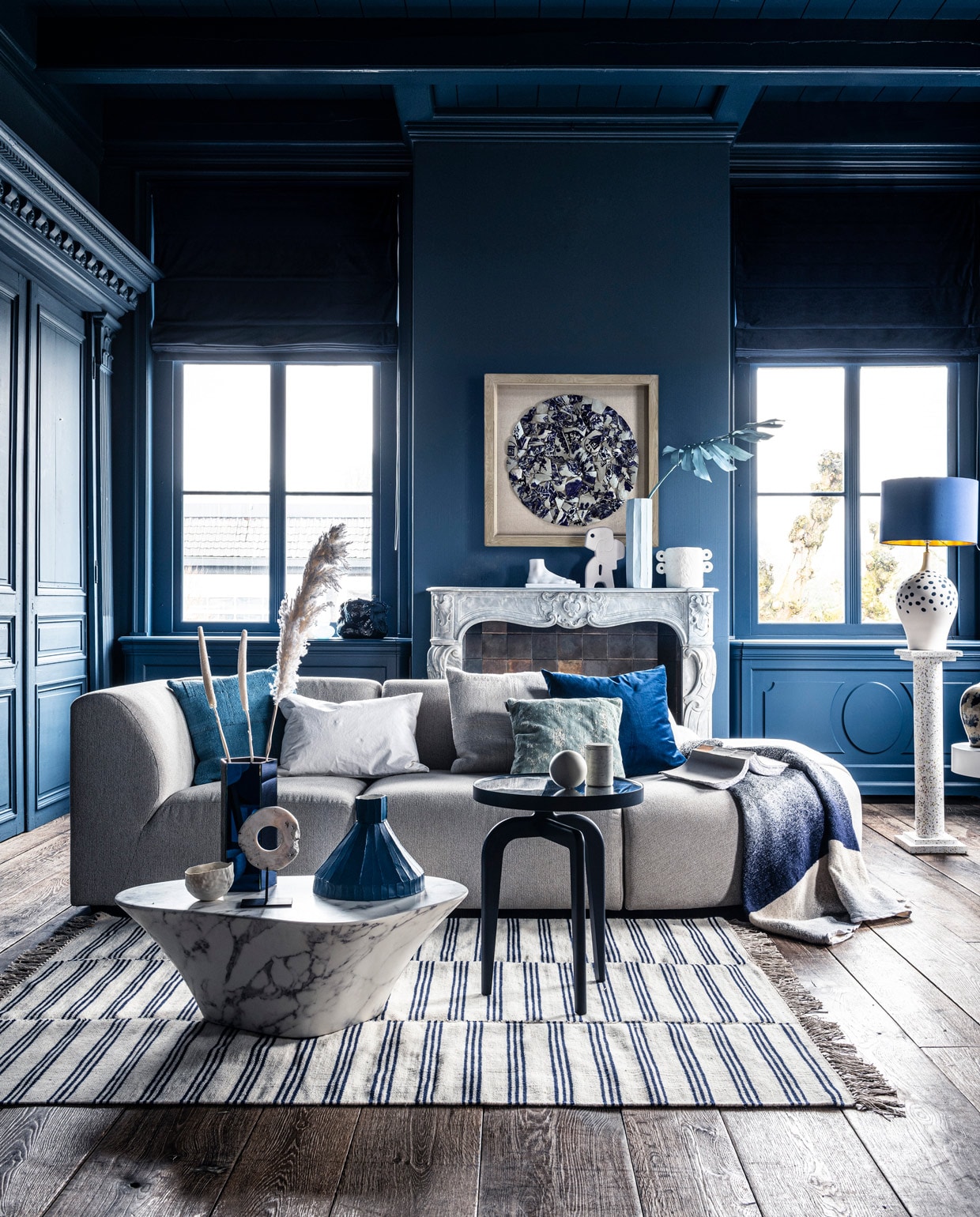 Voet op schouw € 59,95, sierobject op schouw € 58,95, pilaar € 239,-, wit bijzettafeltje € 269,-, witte vaas € 38,35, schilderij prijs op aanvraag (hkliving.nl). Velours stoel € 1200,- (edha-interieur.nl). Kleed € 199,- (zarahome.com). Marmeren salontafel € 587,50, blauwe tak € 57,- (polspotten.nl). Blauwe salontafel Schönbuch € 719,-, plaid Mae Engelgeer € 440,-, wit kussen Mrs.me € 99,- (homestede.nl). Blauw kussen € 49,-, ecru kussen € 49,-, blauw kussen op stoel € 49,- (couleurlocale.eu). Wandlamp It’s about RoMi Chicago € 355,-, kussen Sarona vintage blue 45×45 cm € 35,- (polspotten.nl). Velvet sierkussen 55×55 cm € 74,-, donkerblauwe vaas met tak (klevering.nl), zeshoekige vaas 32 cm hoog € 38,99,-, cockatoo decoratie € 53,- (polspotten.nl), bank Jax hkliving.nl, element vanaf € 499,- (vtwonen.nl). Blauwe vaas, smal toelopend € 469,-, cirkelvormig sierobject € 129,-, wit bankje op tafel, prijs op aanvraag, lichtblauwe vaas 46 cm hoog € 239,-, marmeren pot op blauwe salontafel € 45,-, opengeslagen boek € 40,- (badenbaden.nl). Stoel rechts € 1898,-, sierbal op blauwe tafel, set van 3 € 99,-, houten siervorm op bijzettafel, set van 3 € 99,- (covanderhorst.nl). Schoenen € 34,99 (hm.com). Lampenvoet met stippen € 798,-, gordijnstof 295 cm breed, per meter €103,- (wva.nl). Blauw gevlekte vaas op bijzettafel € 235,95, blauwe kleine pilaar € 66,55, blauwe lampenkap € 332,75, wandbord per twee, € 235,95, marmeren schouw Lodewijk XIV, € 15.125,-, 18e eeuwse houten vloer per m2, € 168,19 (pietjonker.nl). Witte serax vaas op schouw € 40,85 (loods5.nl). Overig privébezit. vtwonen 07-2020 | 	fotografie Sjoerd Eickmans | styling Liza Wassenaar