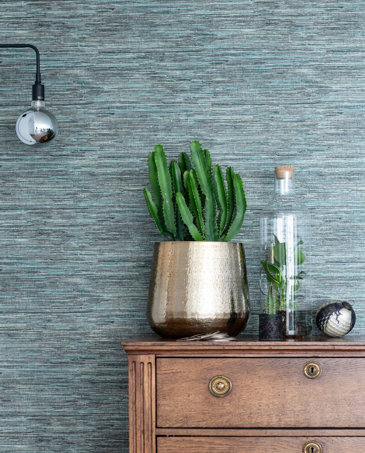 De houten ladekast is een erfstuk. Behang Anthology I Seri Slate via De Mooiste Muren. Goudkleurige bloempot en plant in vaas van Intratuin. Lamp van Menu. vtwonen bk special 03-2020 | binnenkijken Almere