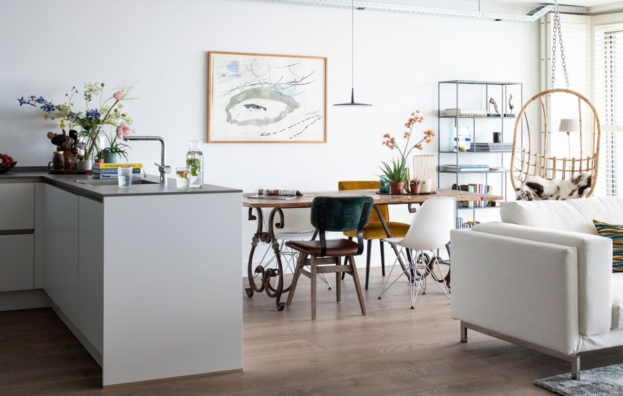 De eettafel is een uniek stuk en niet meer verkrijgbaar. Hanglamp 0270 van Vibia Skan. Witte stoelen DSW van Eames via Vitra. Gele stoel van Woood gekocht bij Karwei. Groen-bruine stoel LifeStyle. Kunstwerk van Meria Bakker. Boekenkast Zuiver. Bank Ikea. vtwonen bk special 03-2020 | binnenkijken Almere
