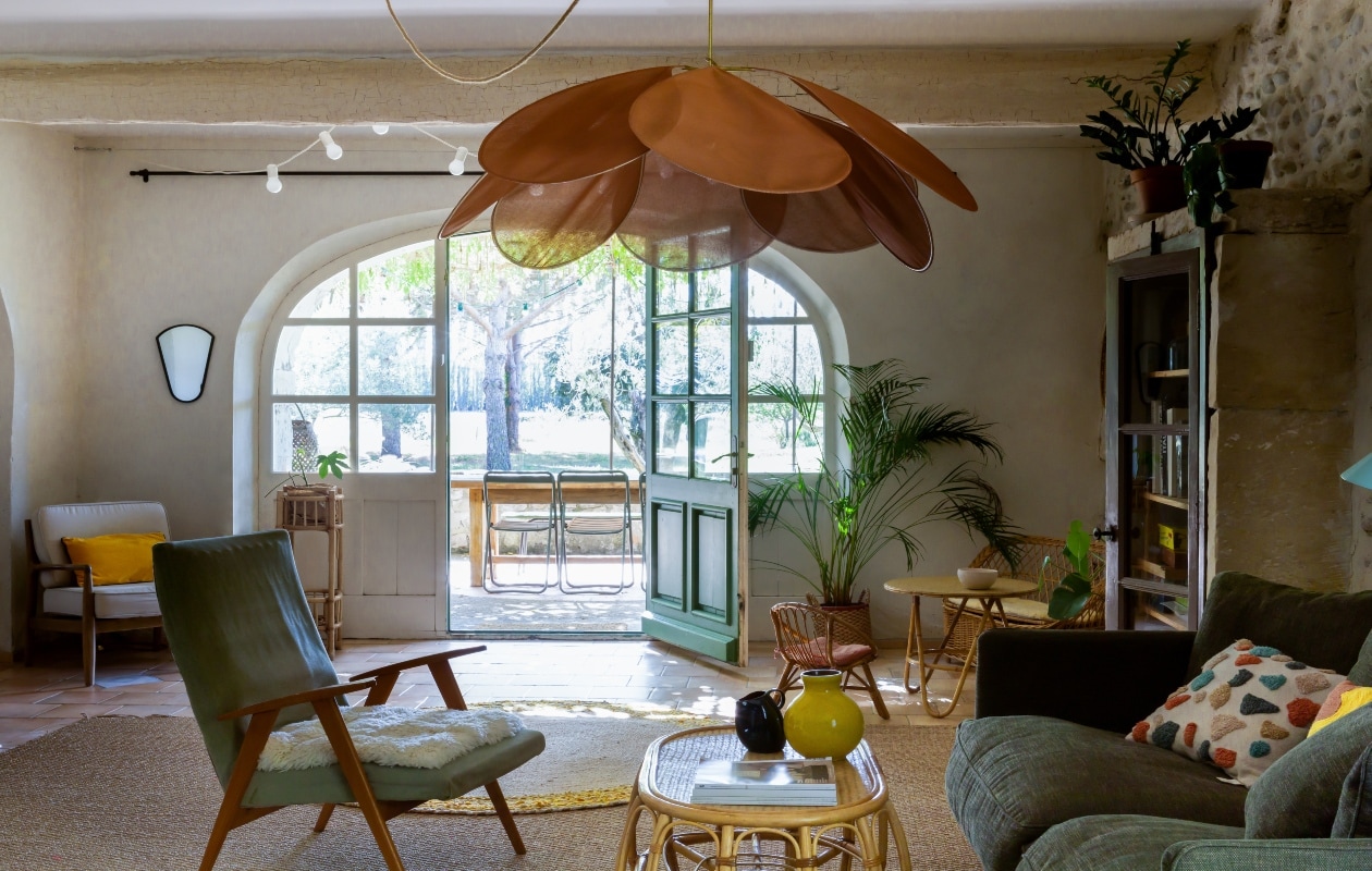 De woonkamer met een mix van retro en rotan elementen. Lamp Georges Store, bank en armstoel Ampm, tafel Hickory, keramiek Ikea en Jars. vtwonen 08-2020 | productie Living Inside | fotografie Monica Spezia