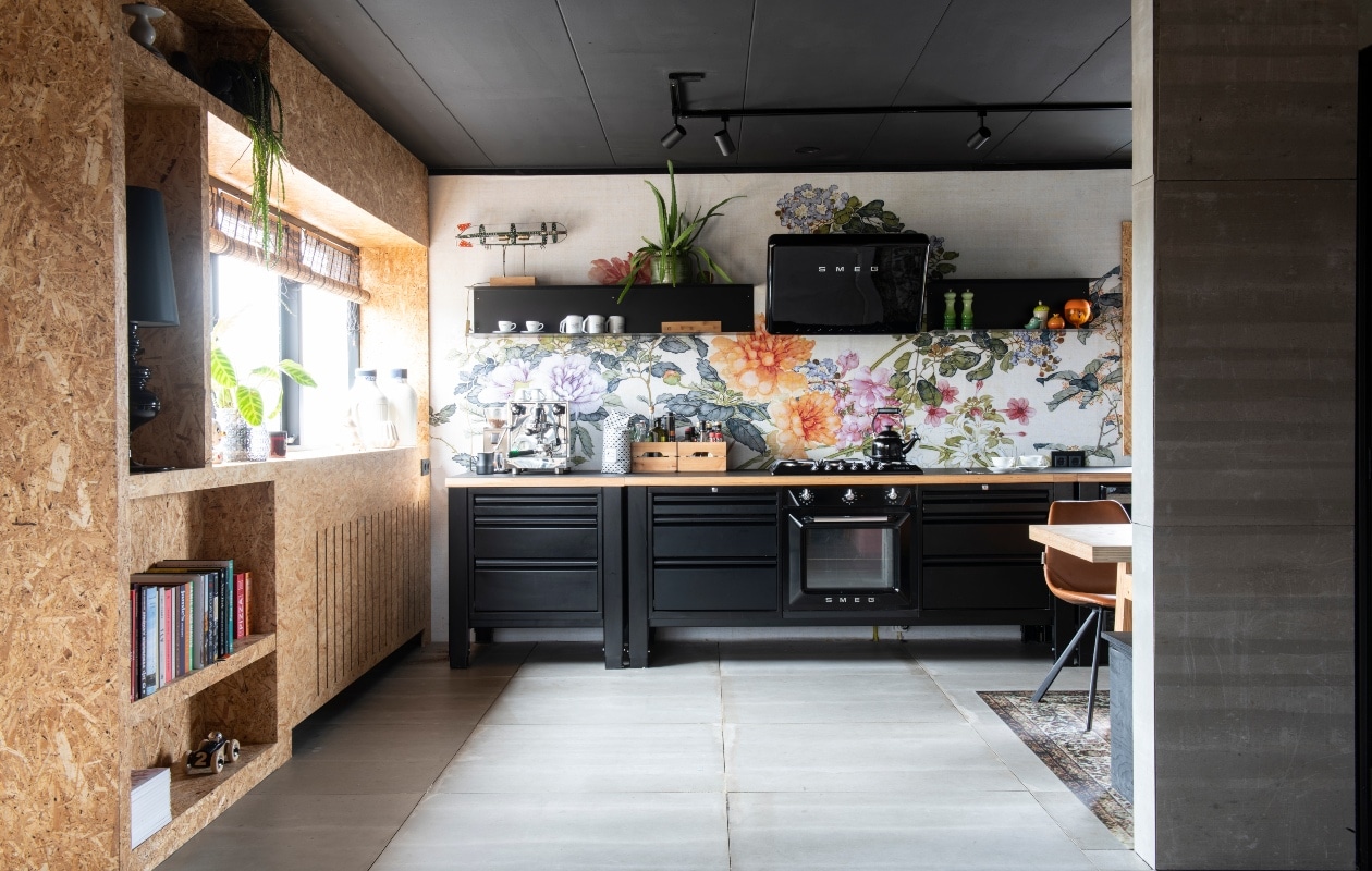 Modulekeuken en keuken – planken via The Big Eeasy Kitchen. Spatwand-behang Kitchen Walls via Behangfabriek. Kast door Rein gemaakt met osb-platen. Stoel Franky Chair van Dutchbone. Vinyl kleed met antisliplaag, zwarte tafellamp en plafondspots Slowclub, wit aardewerk op plank van Rocket, Espresso en Vascobelo. Witte keramieken vazen Royal Delft. Auto in kast Floris Hovers. Lamp op kast gemaakt door Rein van oude Meccano. Groen peper en zoutstel en ketel op fornuis Le Creuset. Espressomachine Rocket. vtwonen binnenkijken 03-2020 | binnenkijken Heerhugowaard