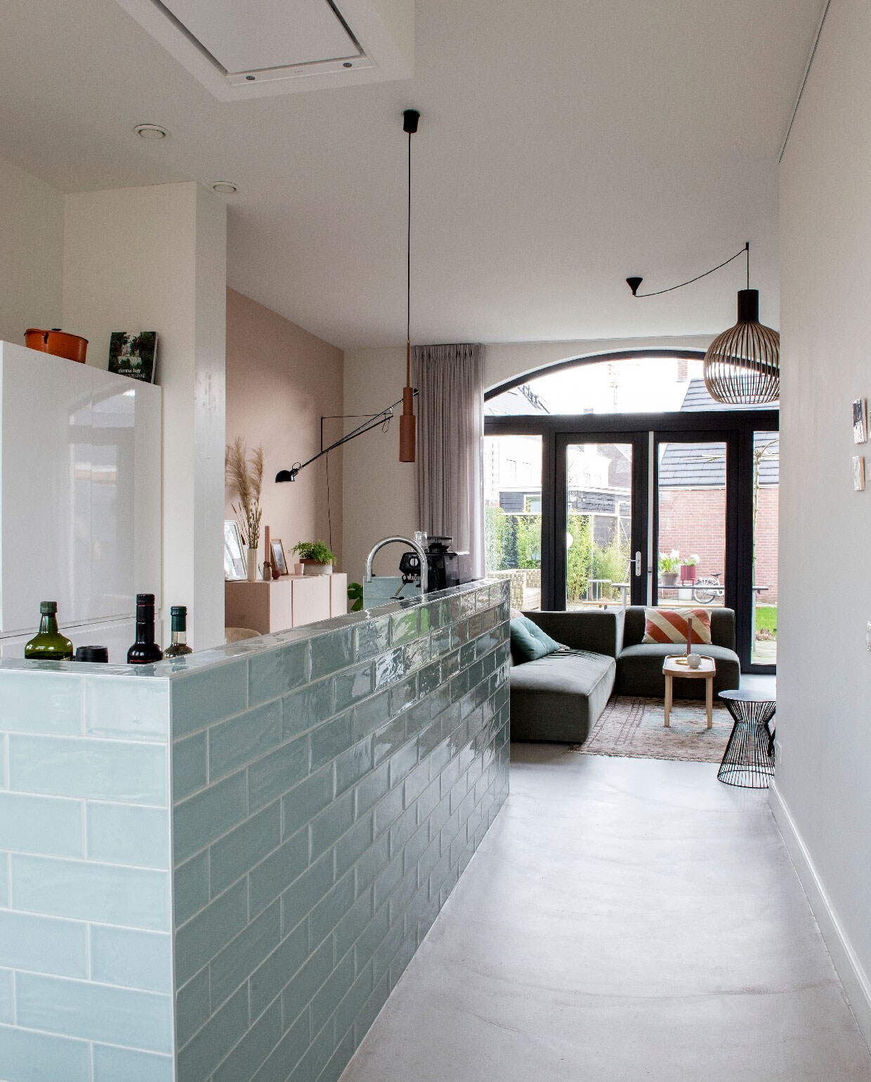 Bank Town van Wehkamp’s Own, kussen op bank HK Living, salontafel Kwantum, houten lamp rechts Secto Design, lamp boven bar Frederik Roijé via vtwonen.nl, wandlamp zwart 265 Flos. Bartegels Aria via Tegels in Huis.
