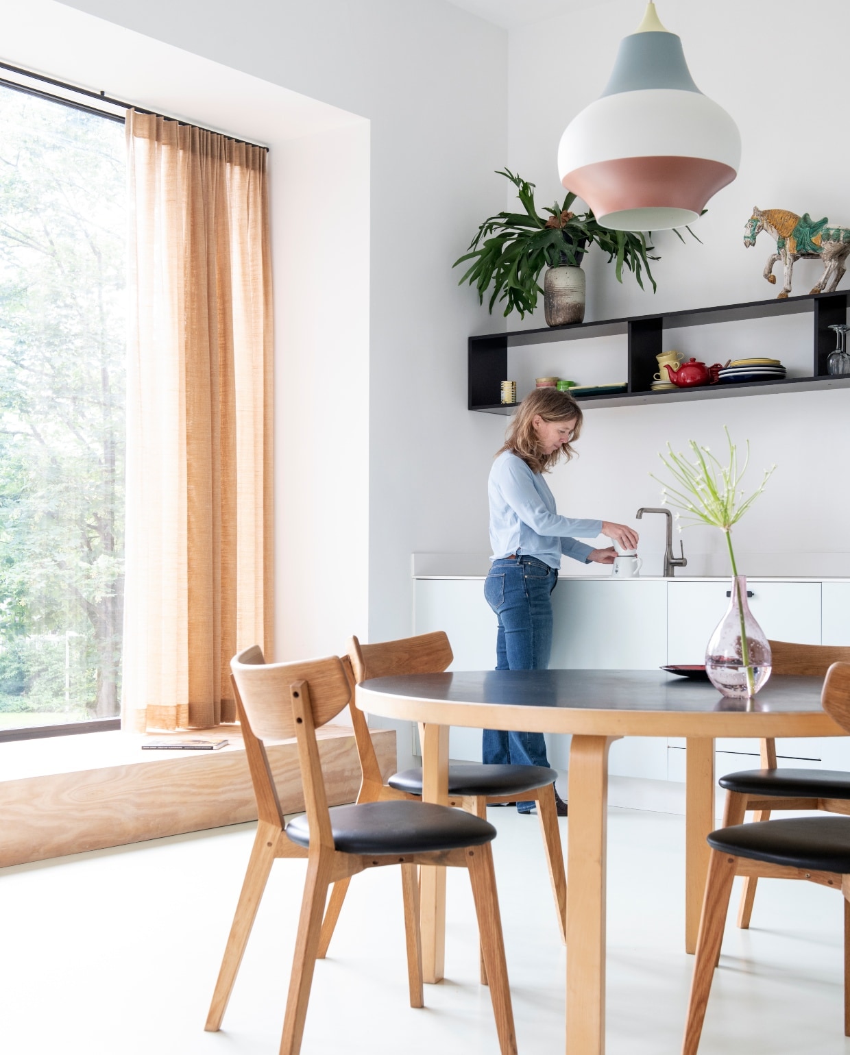 Keukenkasten Kvik. Kleur blauw Pale Powder van Farrow &amp; Ball. Tafel van Artek. Stoelen Ami van Rowico. Erboven Cirque hanglampen van Louis Poulsen. Blauw-roze vaas is een cadeau. Glazen vaas rommelmarkt. Stof gordijnen Jules Sienna van The Alfred Collection. Los element van vintage Artifort bank. Keuken: hanglampen Decovry. Zwart vaasje cadeau gekregen. Het houten art deco tafeltje kreeg Clementine van haar moeder toen ze net op kamers was, het kunstwerk erboven is van Alf Slegers. Fruitschaal van een brocante. vtwonen special 03-2020 | productie InsideHomePage | styling Kristel de Jong | fotografie Louis Lemaire