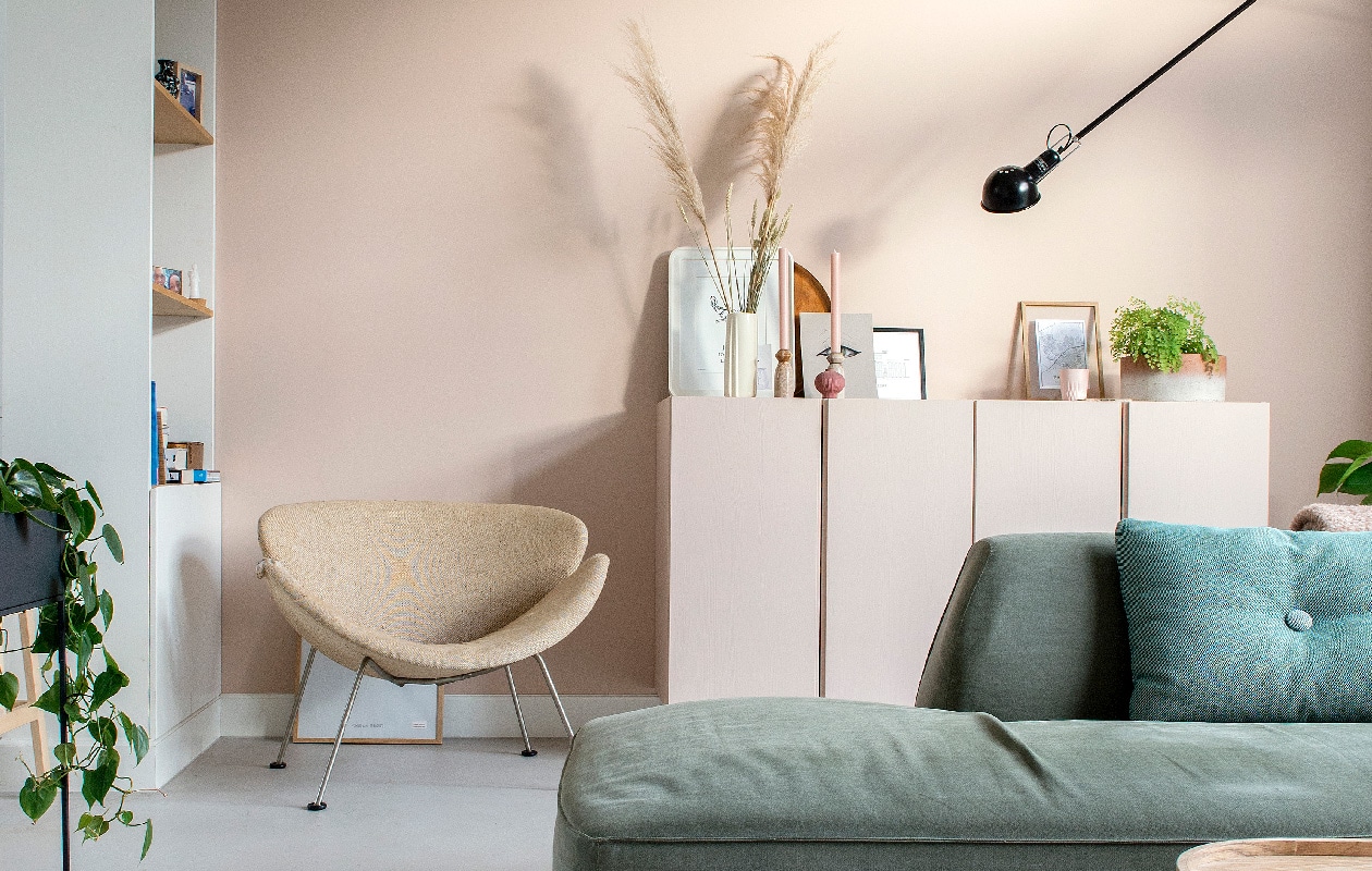 Muurverf Setting Plaster van Farrow &amp; Ball, vloer Leef-Beton gelegd door Het Nieuwe Stenen Tijdperk. Vintage stoel Orange Slice van Artifort Marktplaats. Ikea kastjes geschilderd in de kleur van de muur. Witte fotolijst Ikea, witte vaas en kaarsenhouders kringloop, kaarsen Winand Hazelaar. Print oog gemaakt door dochter Julia, zwarte fotolijst Desenio, houten fotolijst Moebe met daarin in een plattegrond van Zwolle. Herkomst bloempot onbekend, wandlamp 265 Flos, bank Town van Wehkamp’s Own, groen kussen Hay, plaid Blokker, salontafel Kwantum.