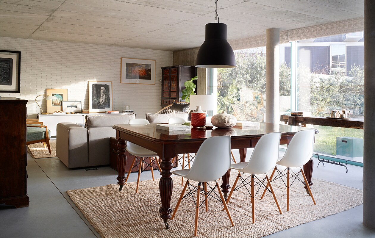 Eettafel en hoge kast antiek. Stoelen DSW van Eames (Vitra). Vazen op tafel Zara Home. Hanglamp en kleed Ikea. Bank en lage kast tegen de muur ontworpen door Marta. De kunstwerken aan de muur en links op de lage kast zijn gemaakt door Marta’s oom Bartolomeu Cid dos Santos. Groot zwart-wit kunstwerk rechts op lage kast Sainer. Blauwe fauteuils vintage.