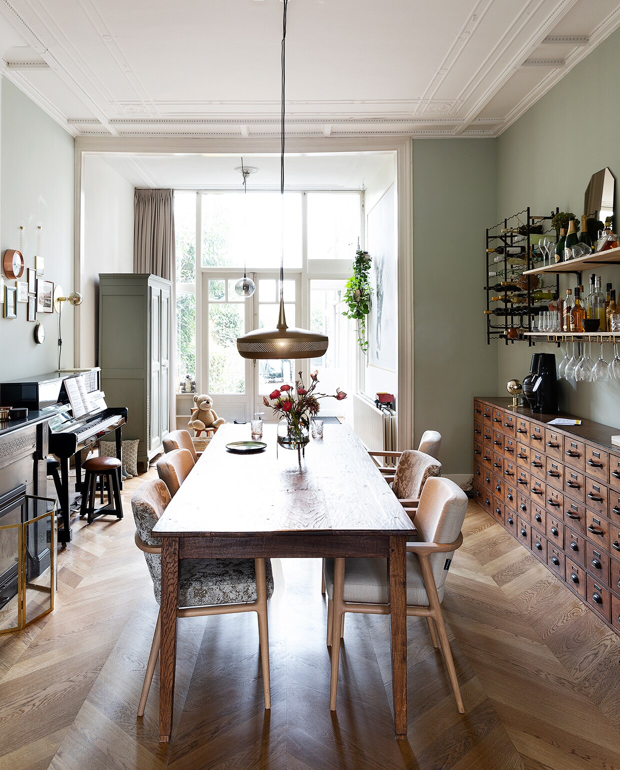Merijn, Stan en Jonah zitten het liefst aan de lange tafel. Ze kregen hem van Merijns ouders. Stoelen Moooi. Hanglamp Umage. Vaas Sissy-Boy. De lichtgroene kast komt uit het huis van Merijns ouders in Frankrijk; Stan en Merijn verfden hem in de kleur Pigeon van Farrow &amp; Ball. Pianokruk Goossens. Kussen Zuiver. Klok Karlsson. Wandlamp Frama. Fotolijsten met kettinkjes Umbra. Plantenhangers Wehkamp. vtwonen 04-2020 | styling Emmy van Dantzig | fotografie Jansje Klazinga | tekst Anne van den Dool