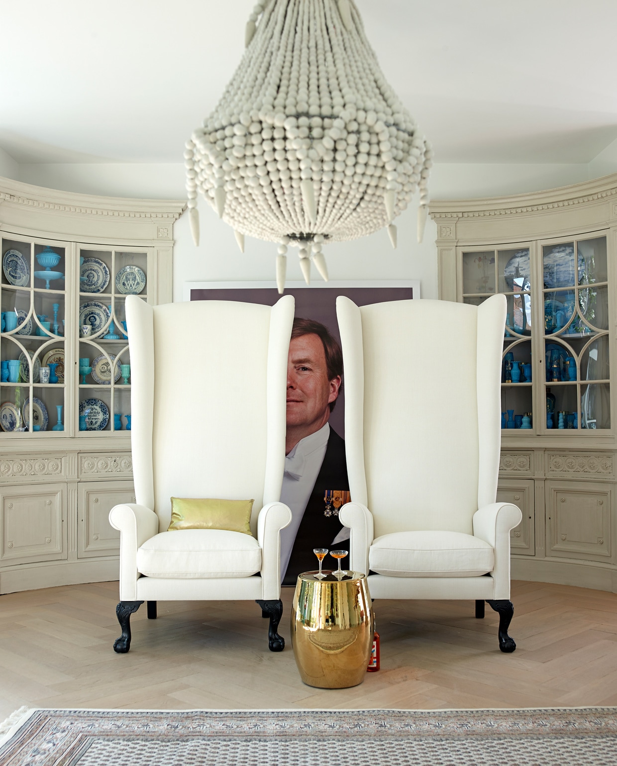 Oorfauteuils met hoge leuning 175 cm hoog Imperial Collection. Portret Zijne Majesteit Koning Willem-Alexander, april 2013 © RVD, foto: Koos Breukel (www.koninklijkhuis.nl). Gouden tafeltje met deksel van Pols Potten Het Arsenaal. Kroonluchter Bodie and Fou. Perzisch kleed Kelim. In de kast antieke borden van Juliana, Beatrix, Wilhelmina en Willem van Kramer. Overig privébezit. vtwonen oktober 2014 | Fotografie Tjitske van Leeuwen | Styling Marianne Luning