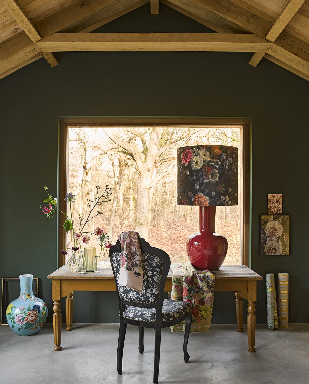 Antieke tafel 160 x 70 x 72 cm cm (lxbxh) (burbri.nl). Lichtblauwe gebloemde vaas, gebloemde lampenkap op rode keramische voet (polspotten.nl). Glazen vaas met bolvormig middenstuk, groene glazen geribbelde vaas (hkliving.nl). Kleine bolvormige vaas met reliëf, glazen flesjes (Waterdrinker). Grote bolvormige vaas (loods5.nl). Tafelkleed, theedoek (brechtjeolsthoorn.nl). Poster met rozen Bild in lijst Ribba, 30×40 cm (bxh) (ikea.nl). Kleine afbeelding privé. Stoel (hetgoed.nl). Gebloemd behang en gestreept behang van Pip Studio (eijffinger.com).